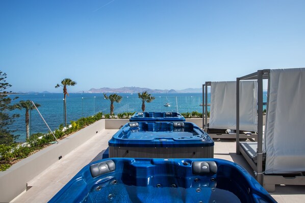 Zona de piscina con jacuzzis y sillas de descanso con vistas al mar.