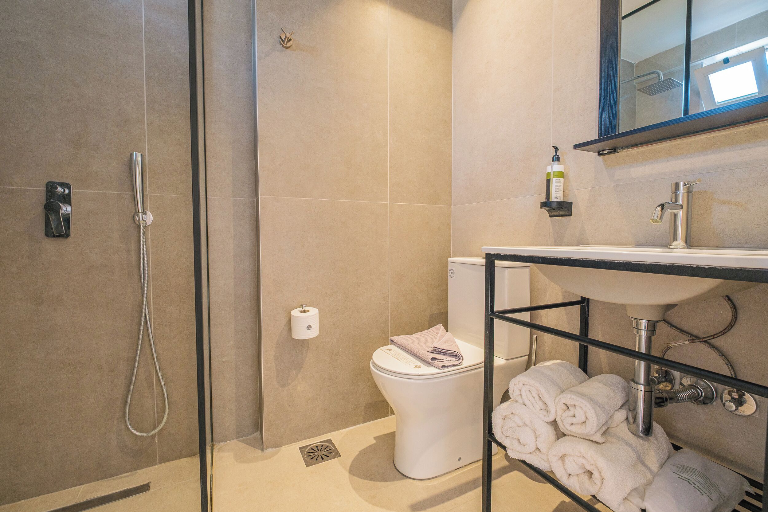 A bathroom with a glass-enclosed shower, a toilet, and a sink with a towel rack.