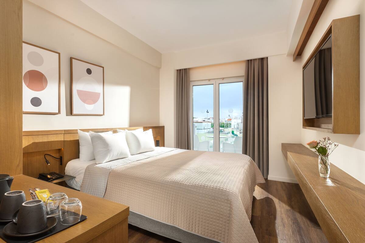 A hotel room with a bed, a desk with a coffee maker, a TV, and a window with a city view.