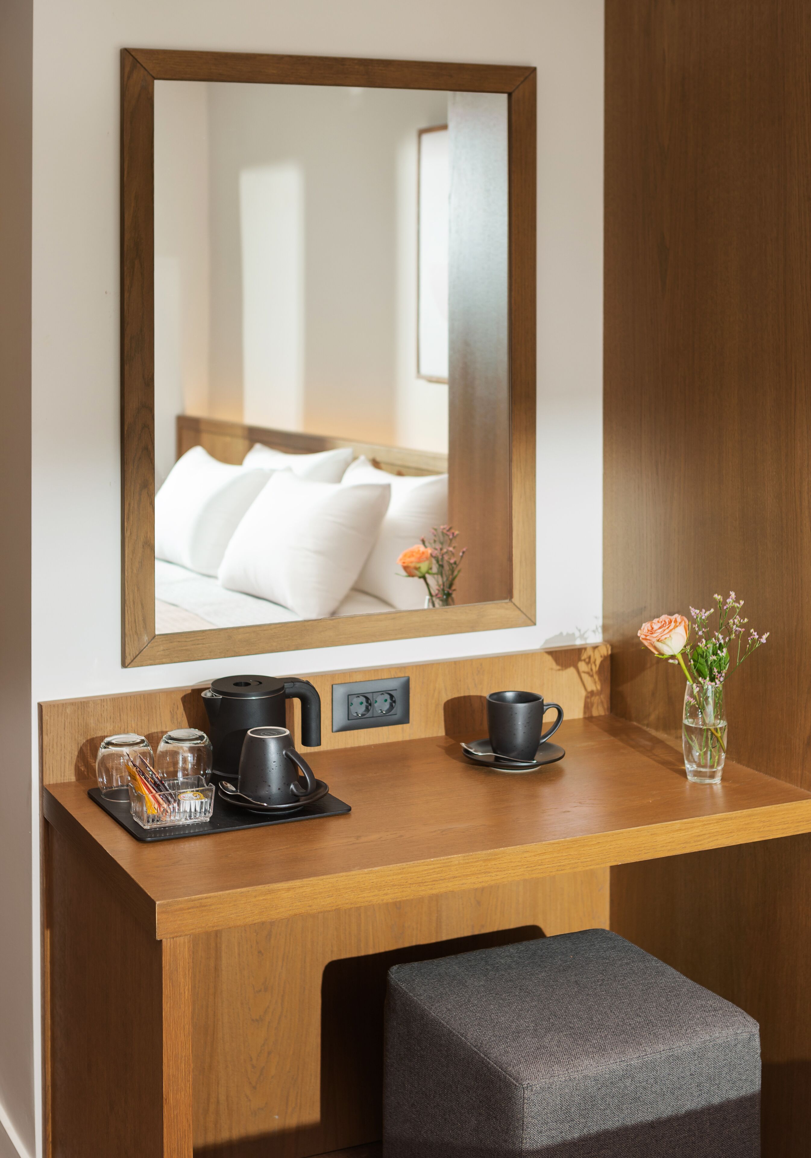 Un bureau en bois avec un miroir, un vase rempli de fleurs et un ensemble pour préparer du café.
