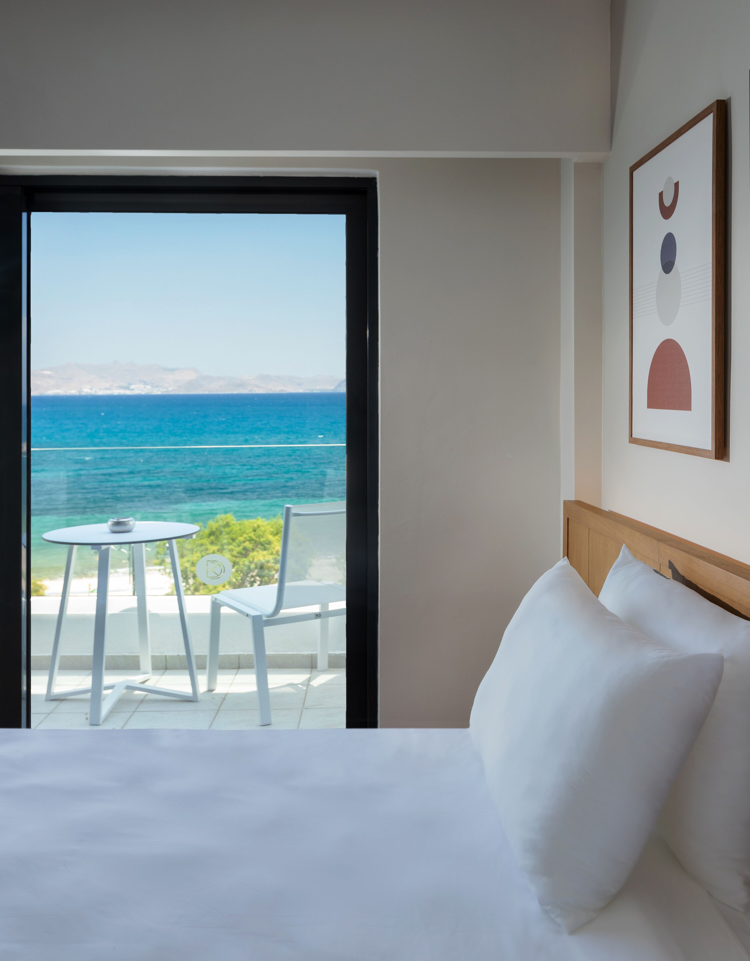 Habitación de hotel con una cama, vista al océano, una mesita y dos sillas.