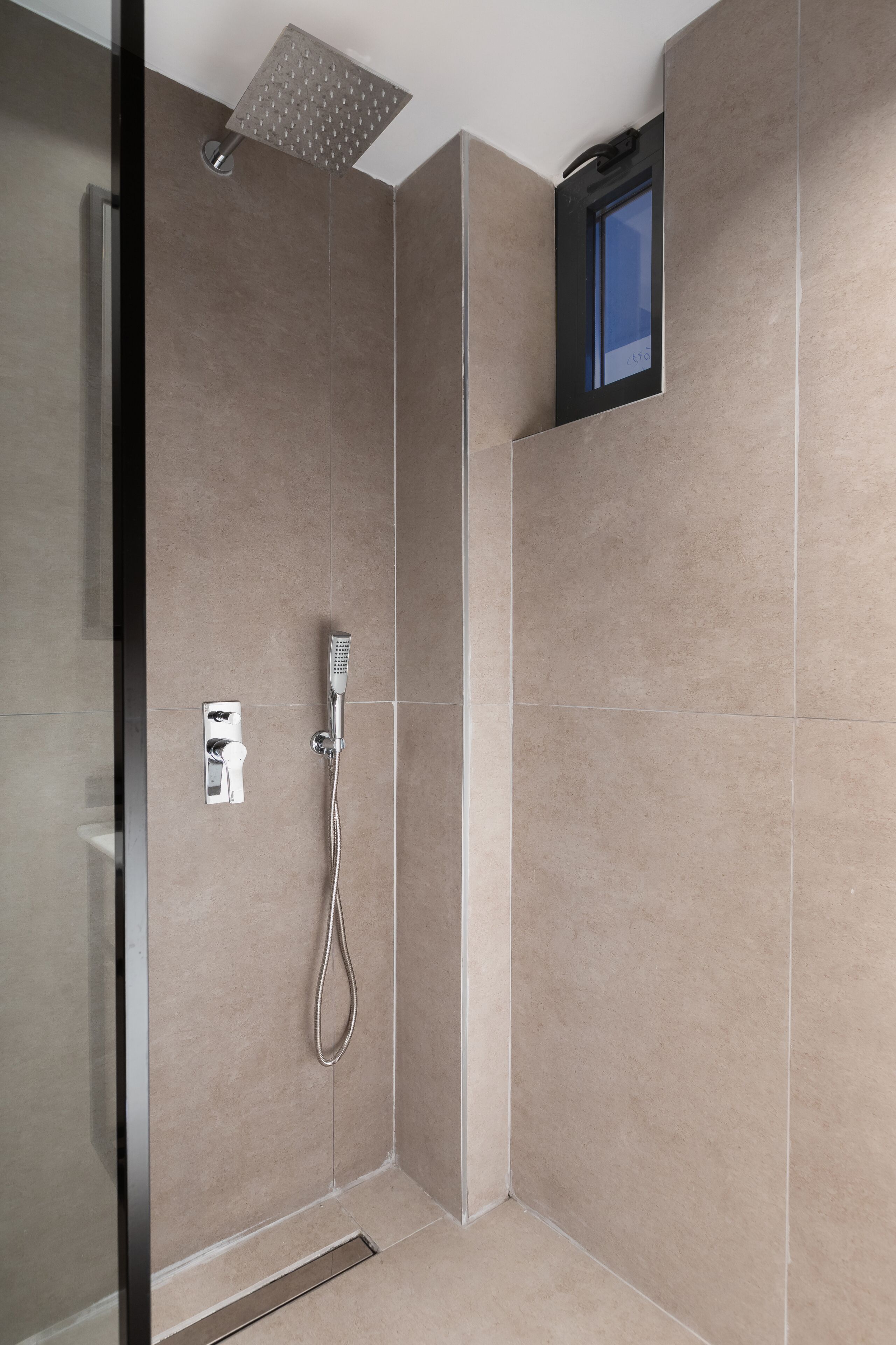 A modern bathroom with a glass shower enclosure, a handheld showerhead, and a wall-mounted control panel.