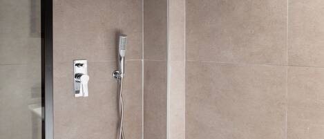 A modern bathroom with a glass shower enclosure, a handheld showerhead, and a wall-mounted control panel.
