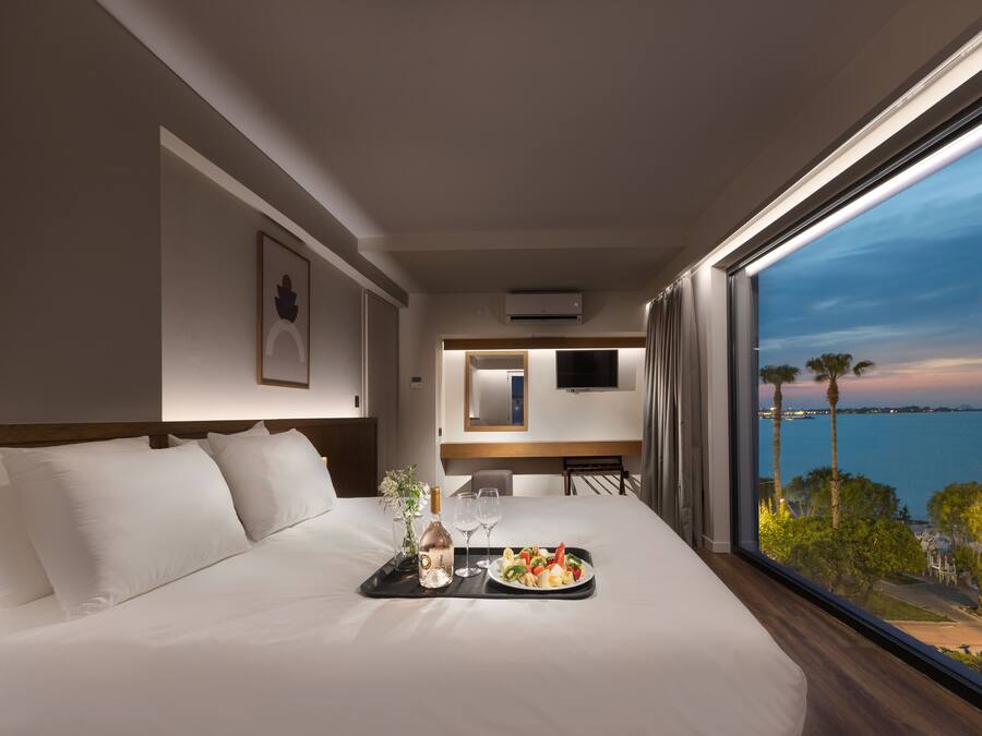 A hotel room with a bed, a tray with a bottle and glasses, and a view of the sea.