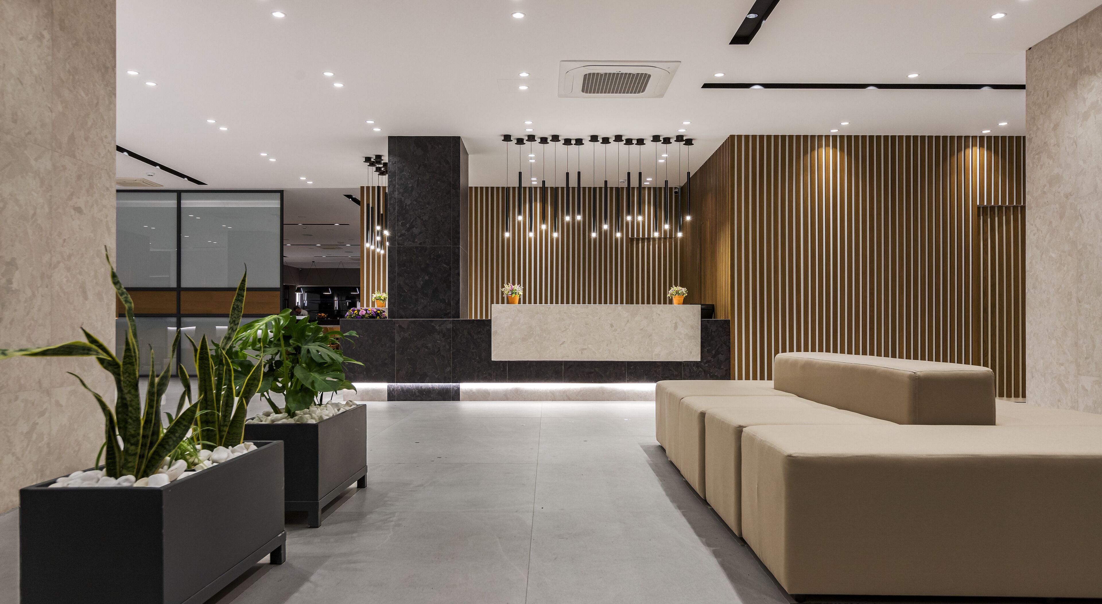 Uma área de recepção moderna, com balcão, assentos e plantas decorativas.