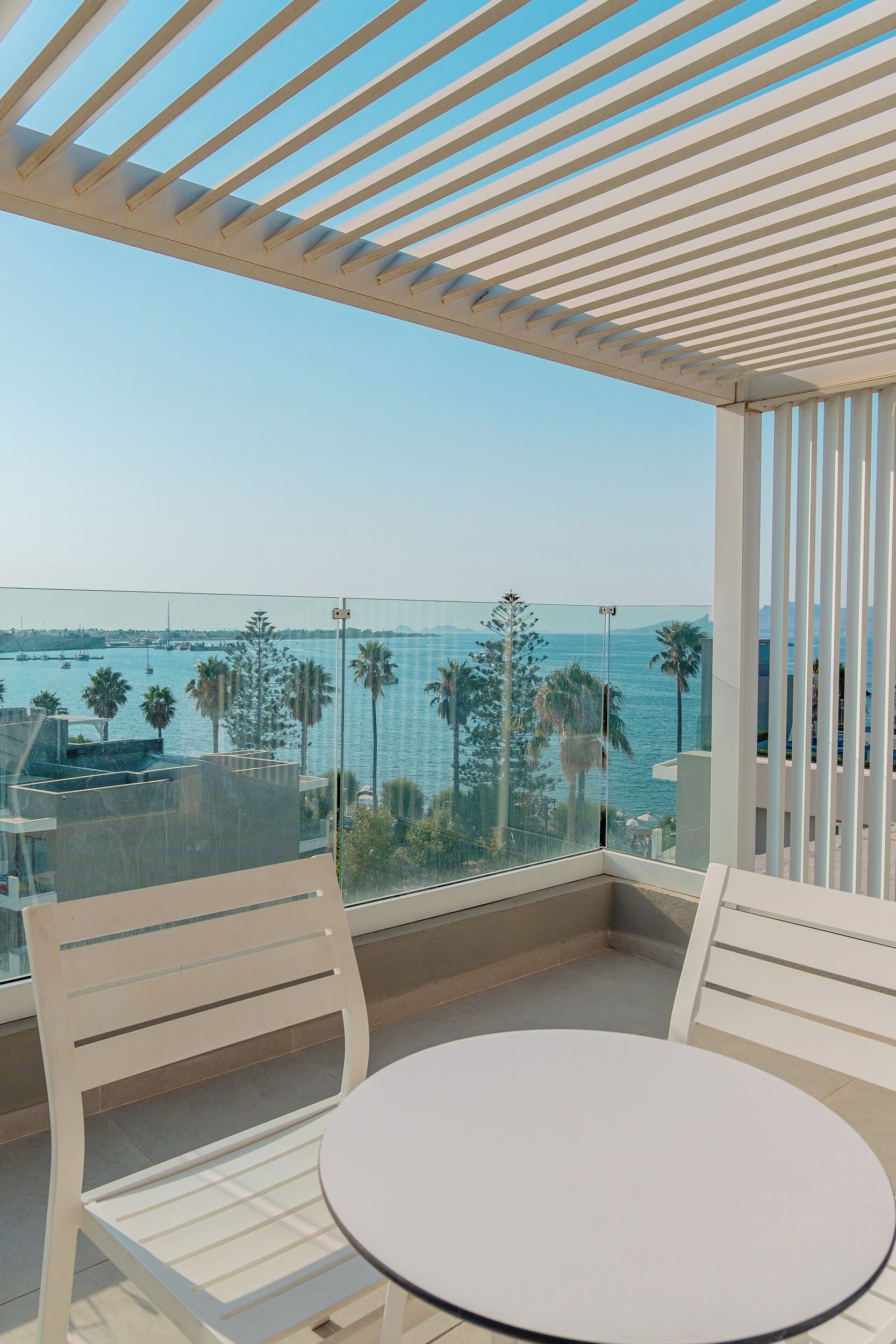 A balcony with a glass railing, white chairs, and a round table.