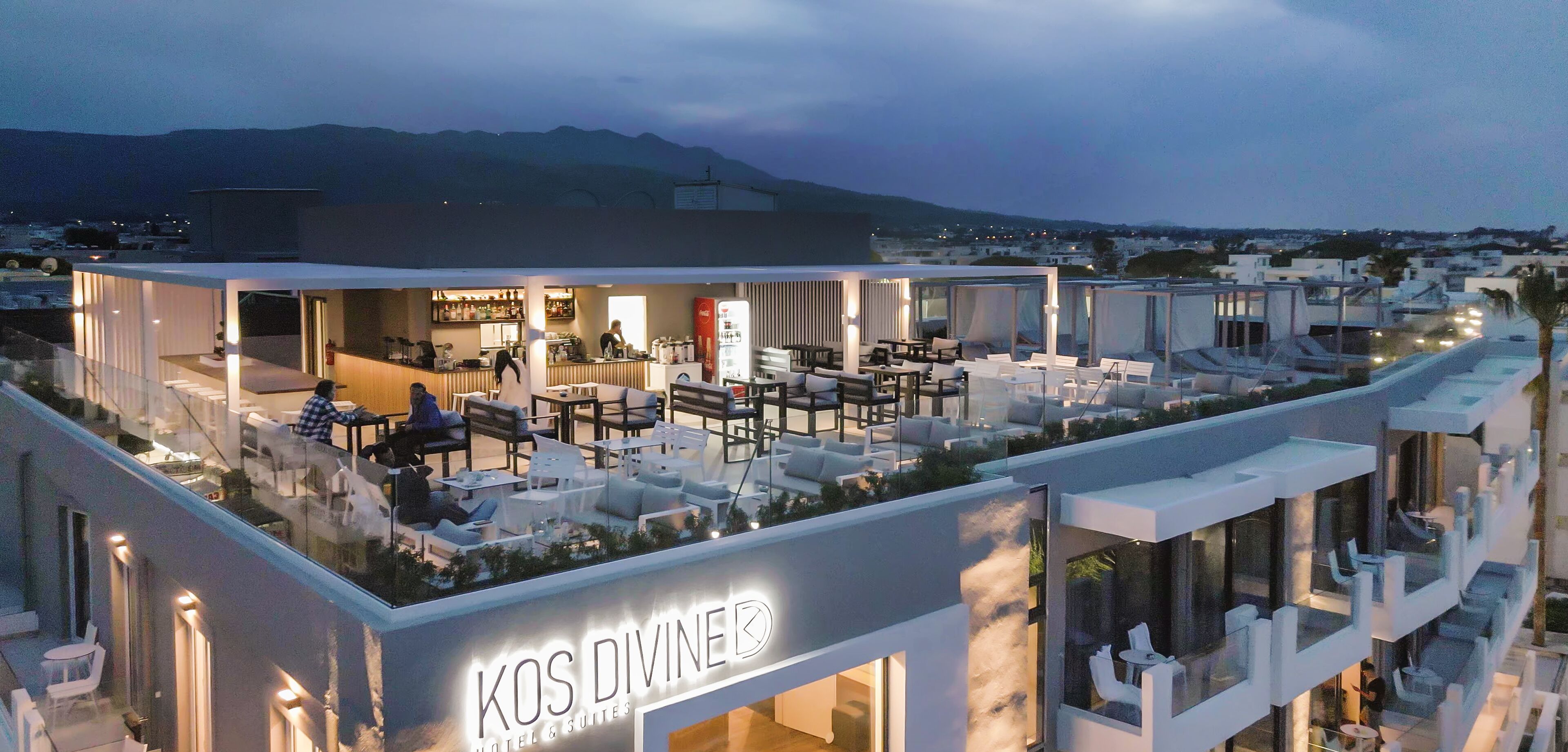 A hotel with a rooftop bar, outdoor seating, and a view of the mountains.
