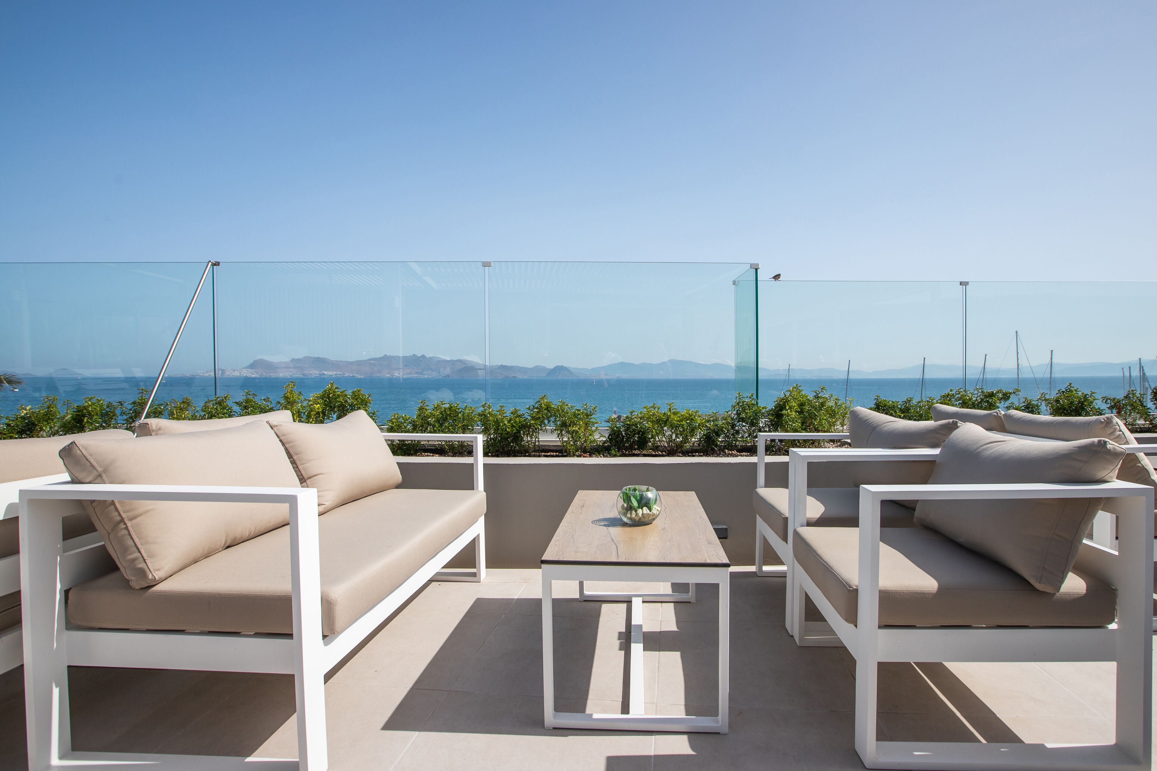 Terraza en la azotea con vistas despejadas al mar y montañas a lo lejos. Hay dos sofás blancos y una mesita con un cuenco.