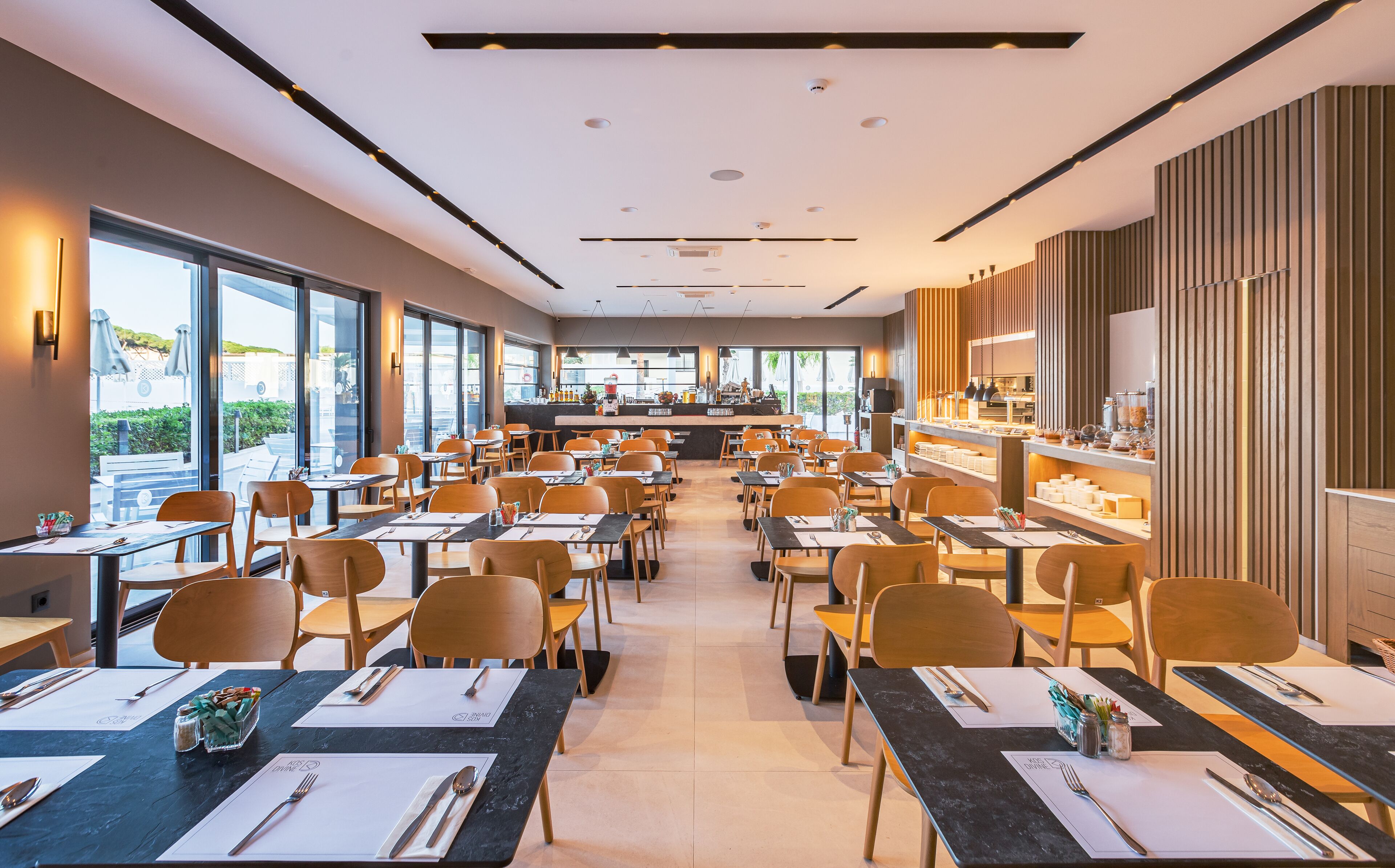 A spacious restaurant with multiple tables and chairs, a bar area, and large windows offering a view of the outdoors.
