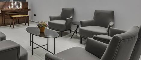 A modern living room with grey sofas, a coffee table, and a piano.