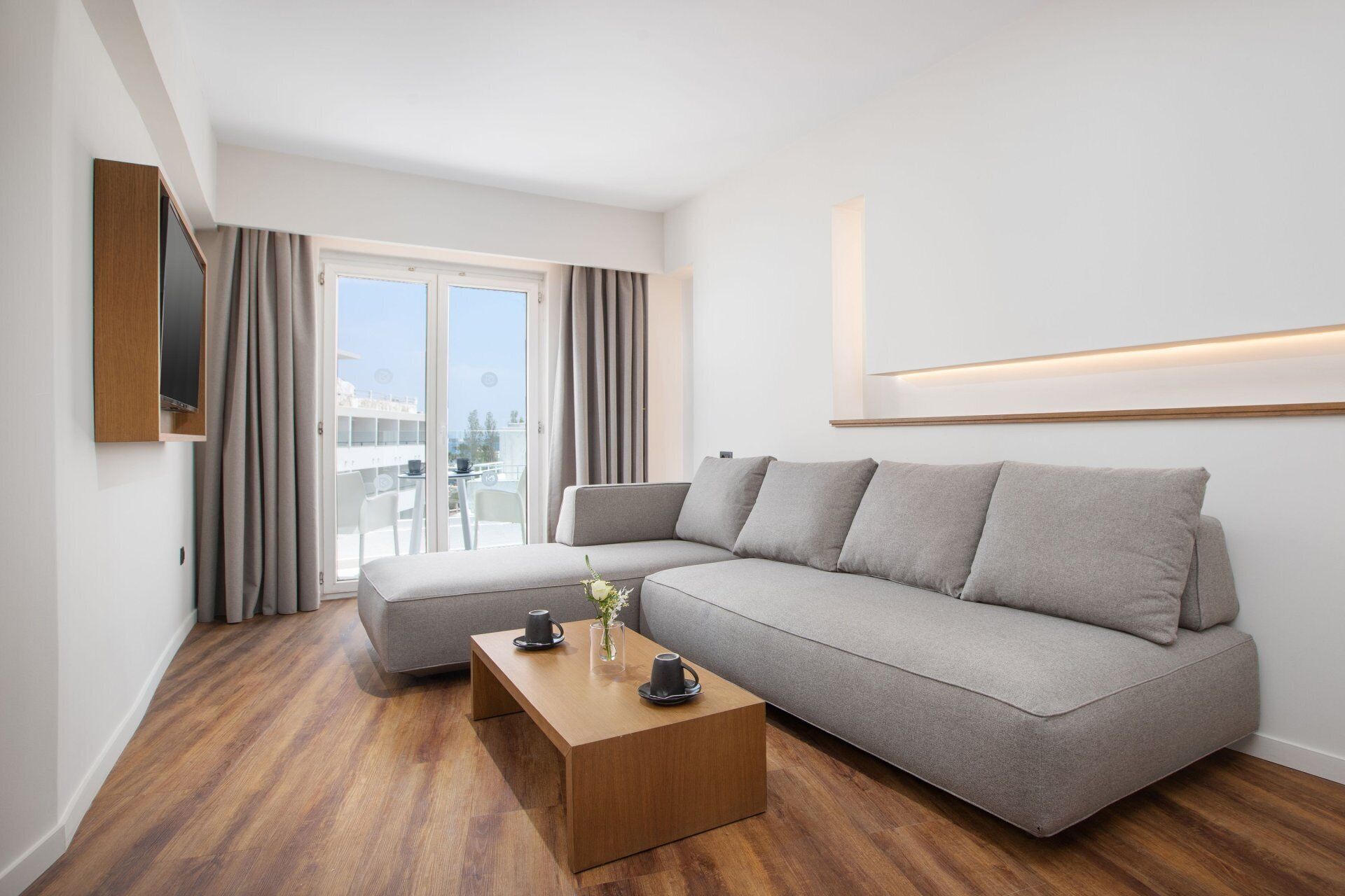 Un salon moderne avec un canapé gris, une table basse en bois et un balcon agrémenté de chaises blanches.