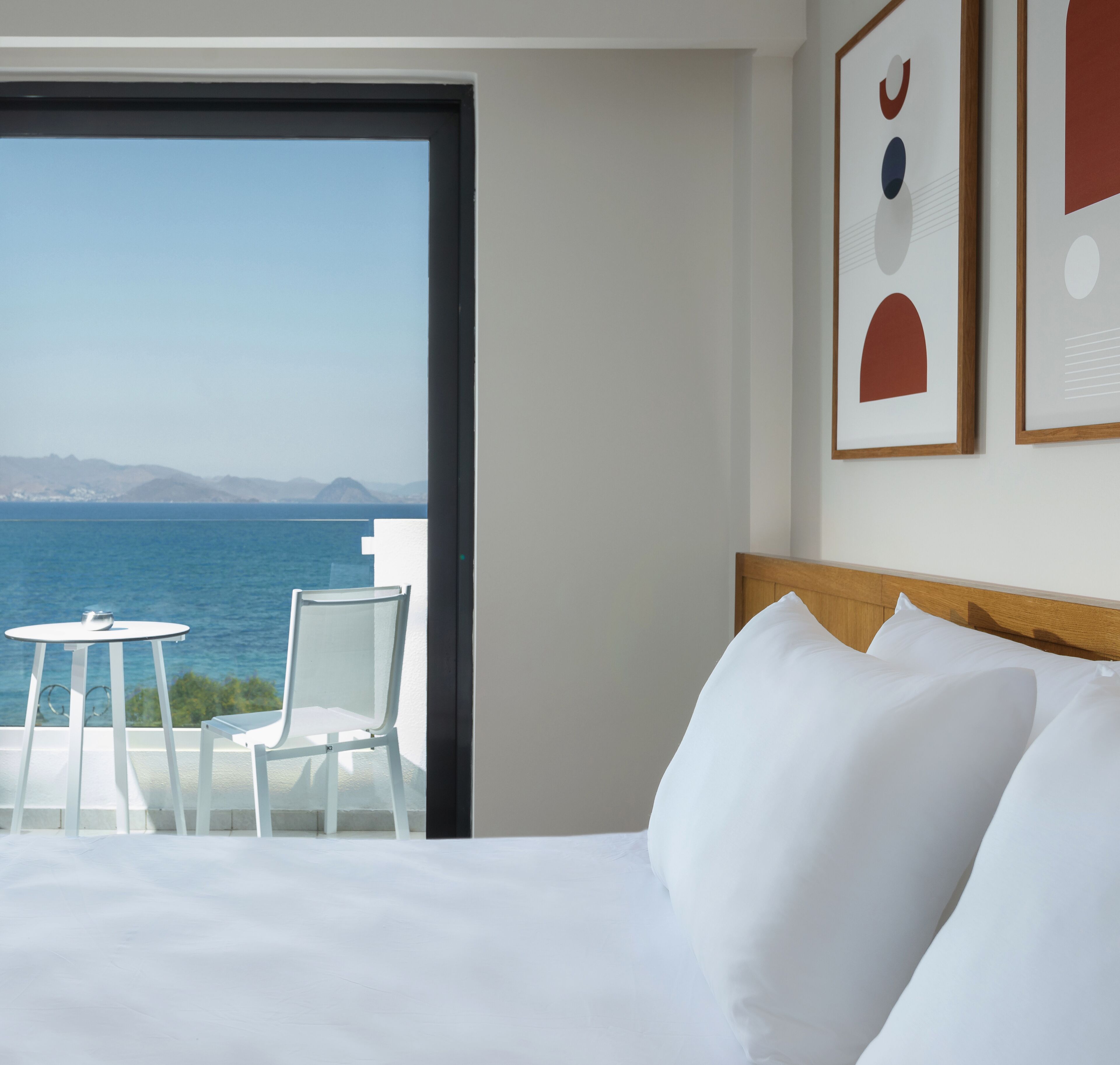 Habitación de hotel con cama, una mesita, dos sillas y vista al mar.