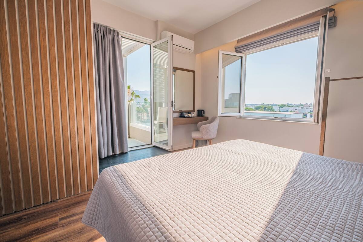 A hotel room with a bed, a chair, a window, and a view of the city.