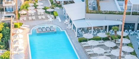 Eine Luftaufnahme eines Resorts mit einem Schwimmbad, Liegestühlen und Palmen.