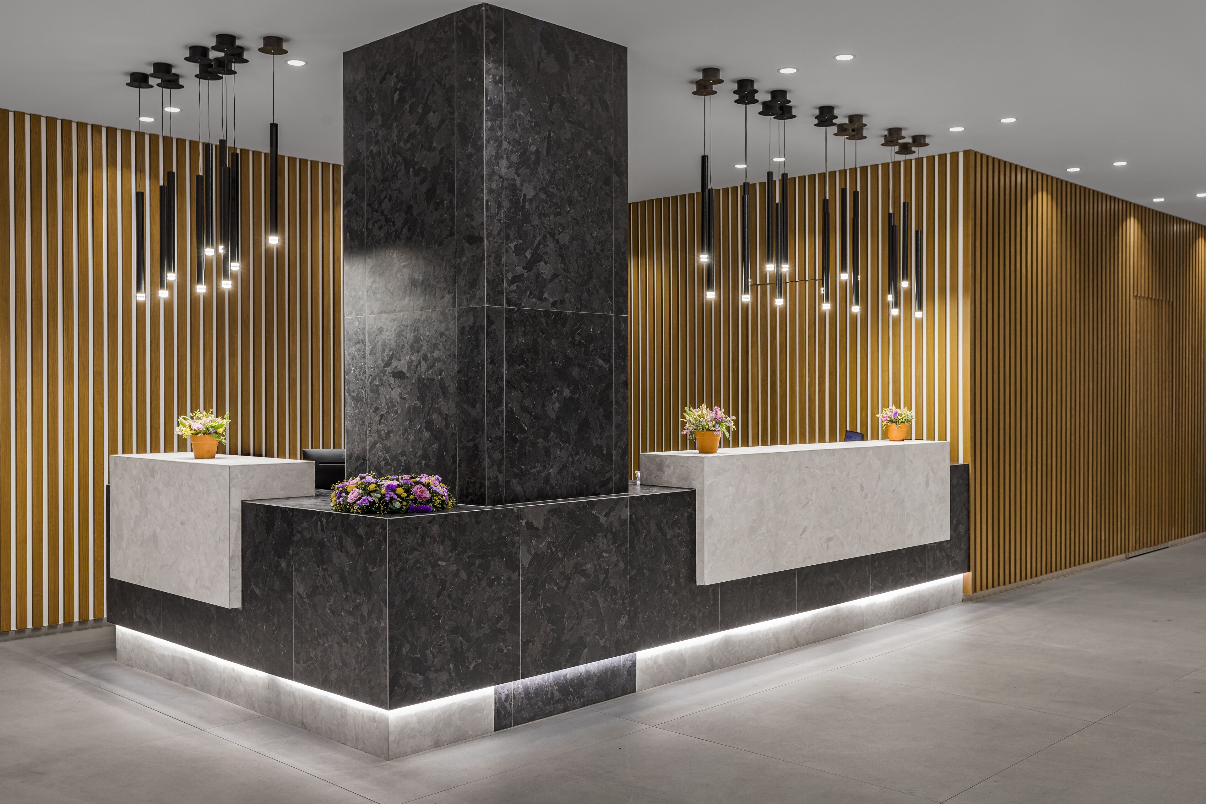 A reception area with a marble reception desk, vertical wooden slats, and pendant lighting.