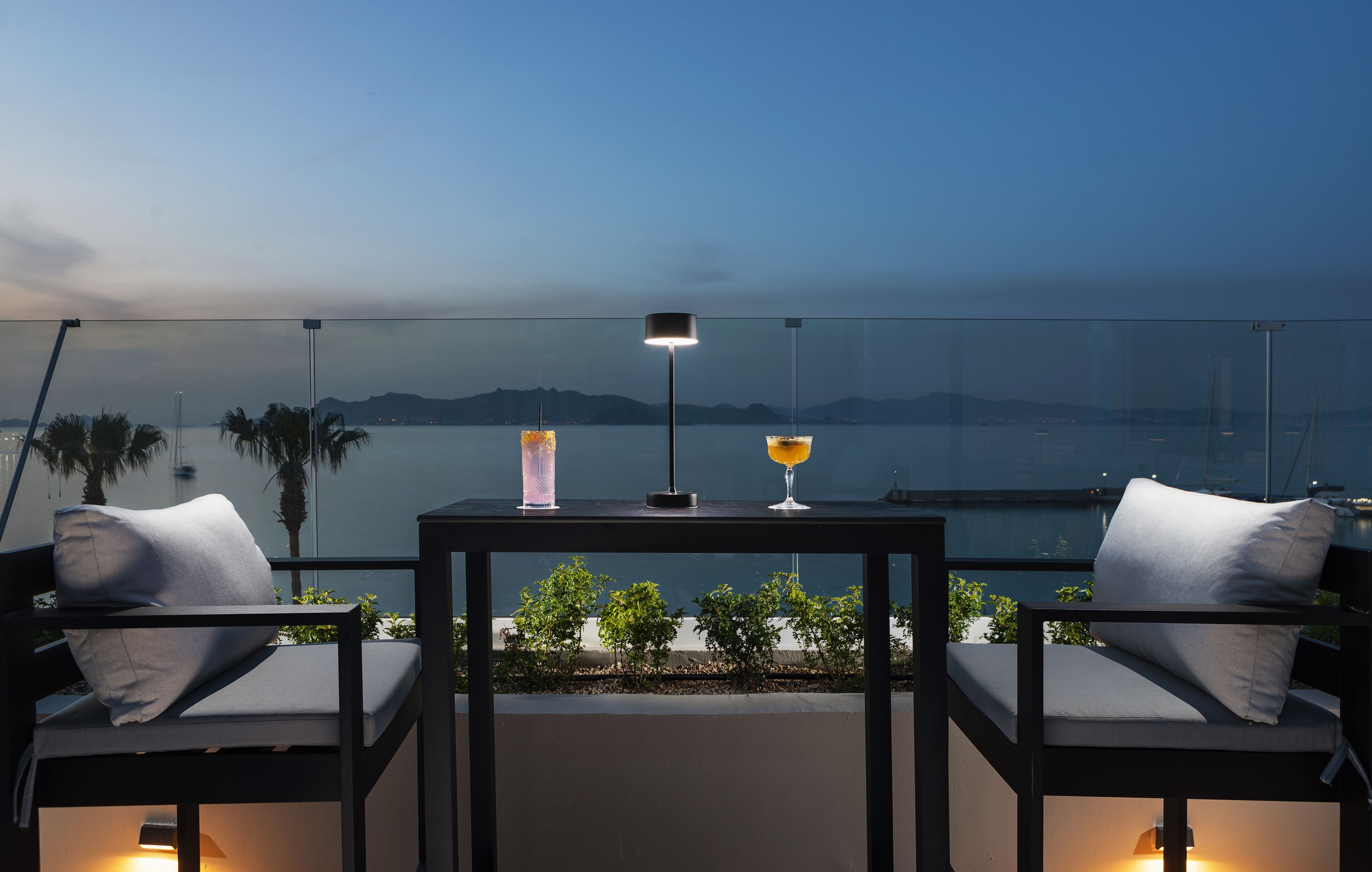A balcony with two chairs, a table, and two drinks.