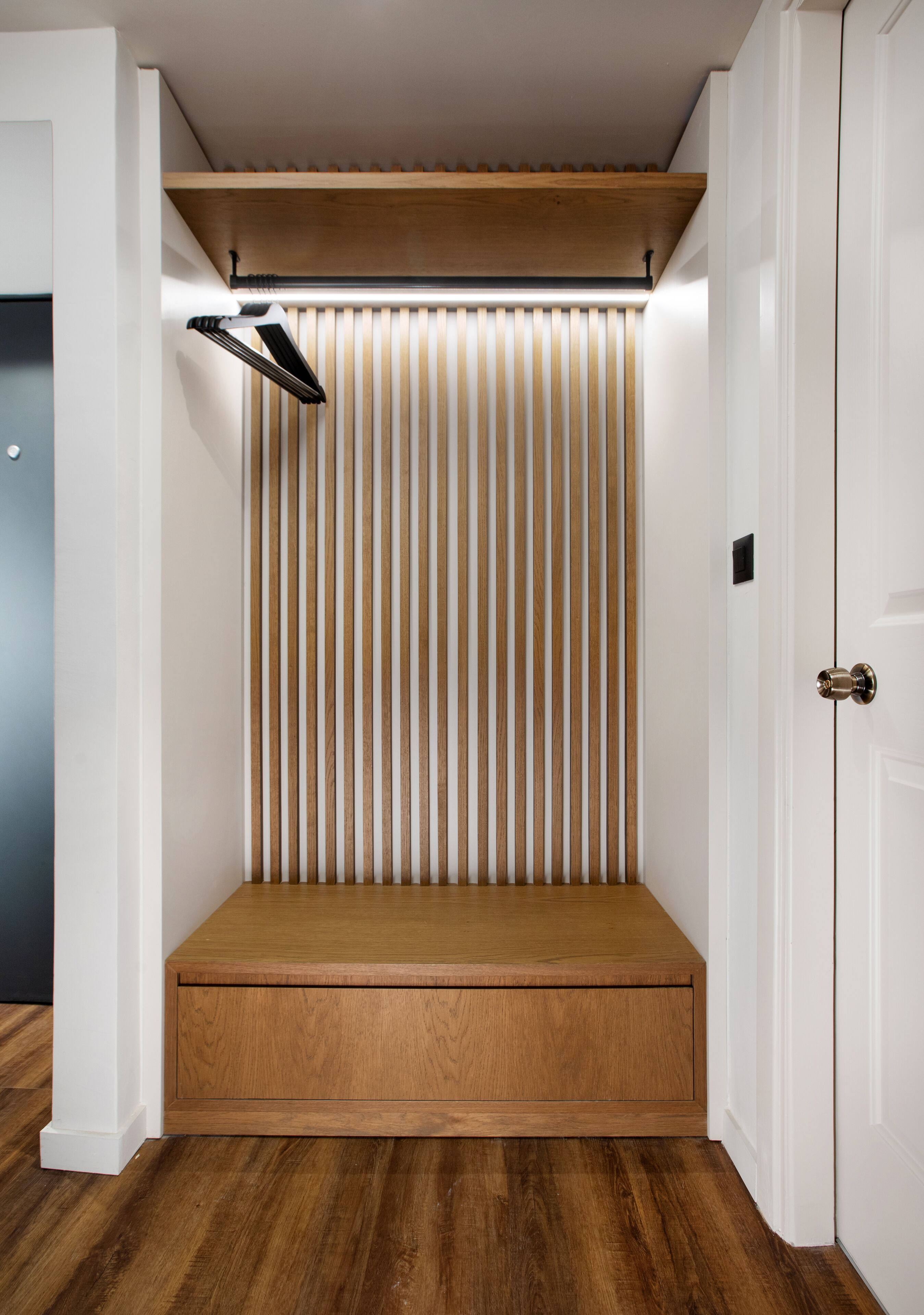 A compact room with a built-in bench, vertical blinds, and a ceiling-mounted light fixture.