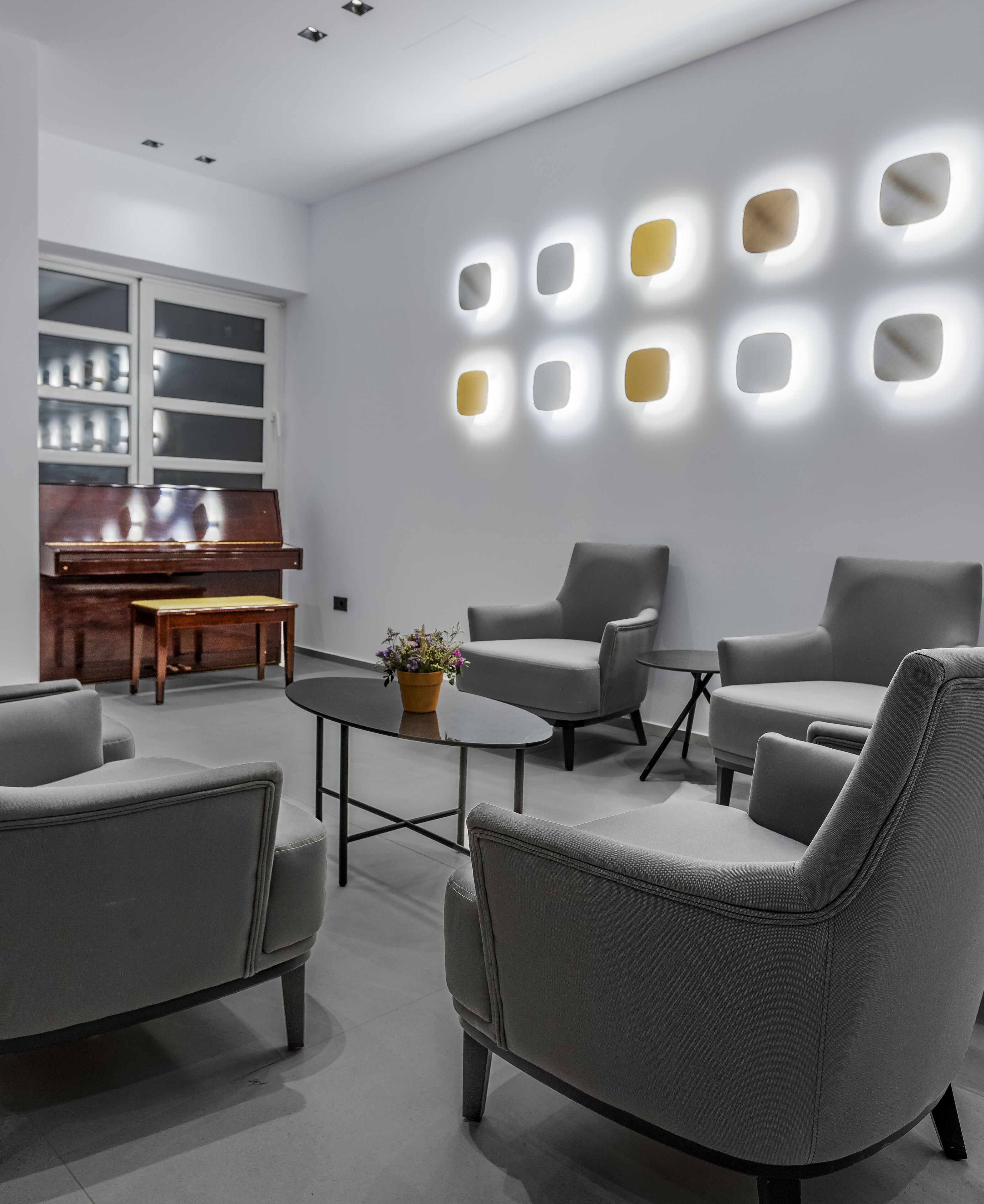 A modern living room with grey sofas, a piano, and a wall with illuminated square lights.