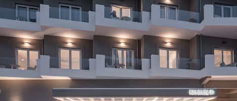 Un hôtel moderne à plusieurs étages, doté de balcons, d’un espace de réception et d’un magasin bien visible appelé « KOS DIVINE ».