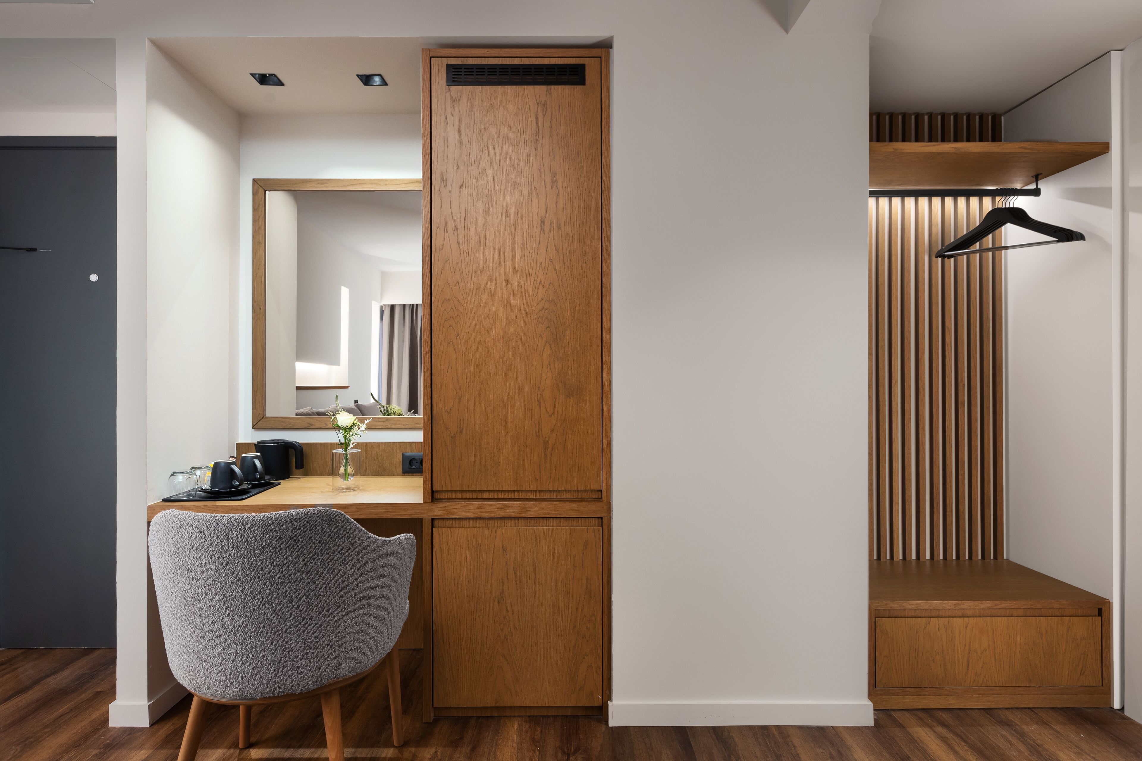 A modern room with a wooden desk, a chair, a mirror, and a hanging rack.