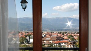 A view through a window with a hanging lamp, showcasing a town with red-roofed buildings and mountains in the background. - All Seasons Club (Bansko)