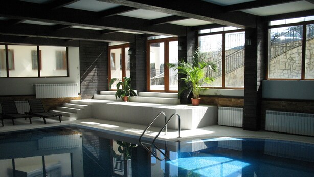 An indoor swimming pool with clear glass walls, a set of stairs leading to a seating area, and potted plants. - All Seasons Club (Bansko)