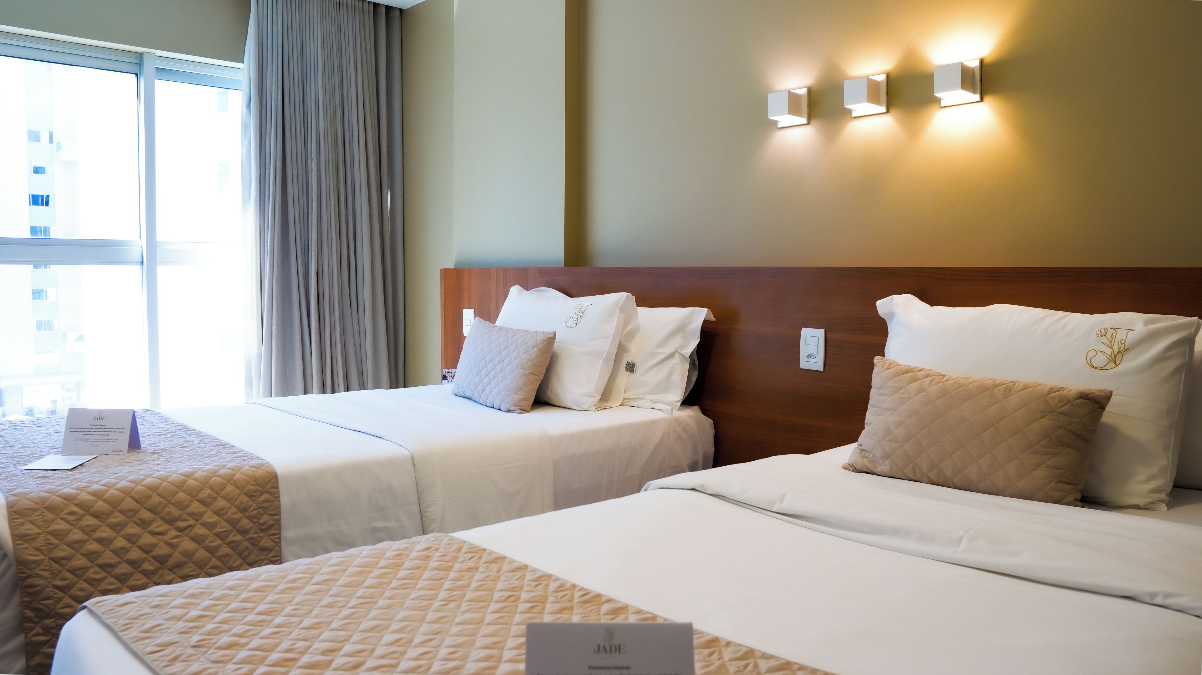 Une chambre d’hôtel avec deux lits, une fenêtre avec des rideaux et un luminaire fixé au mur.