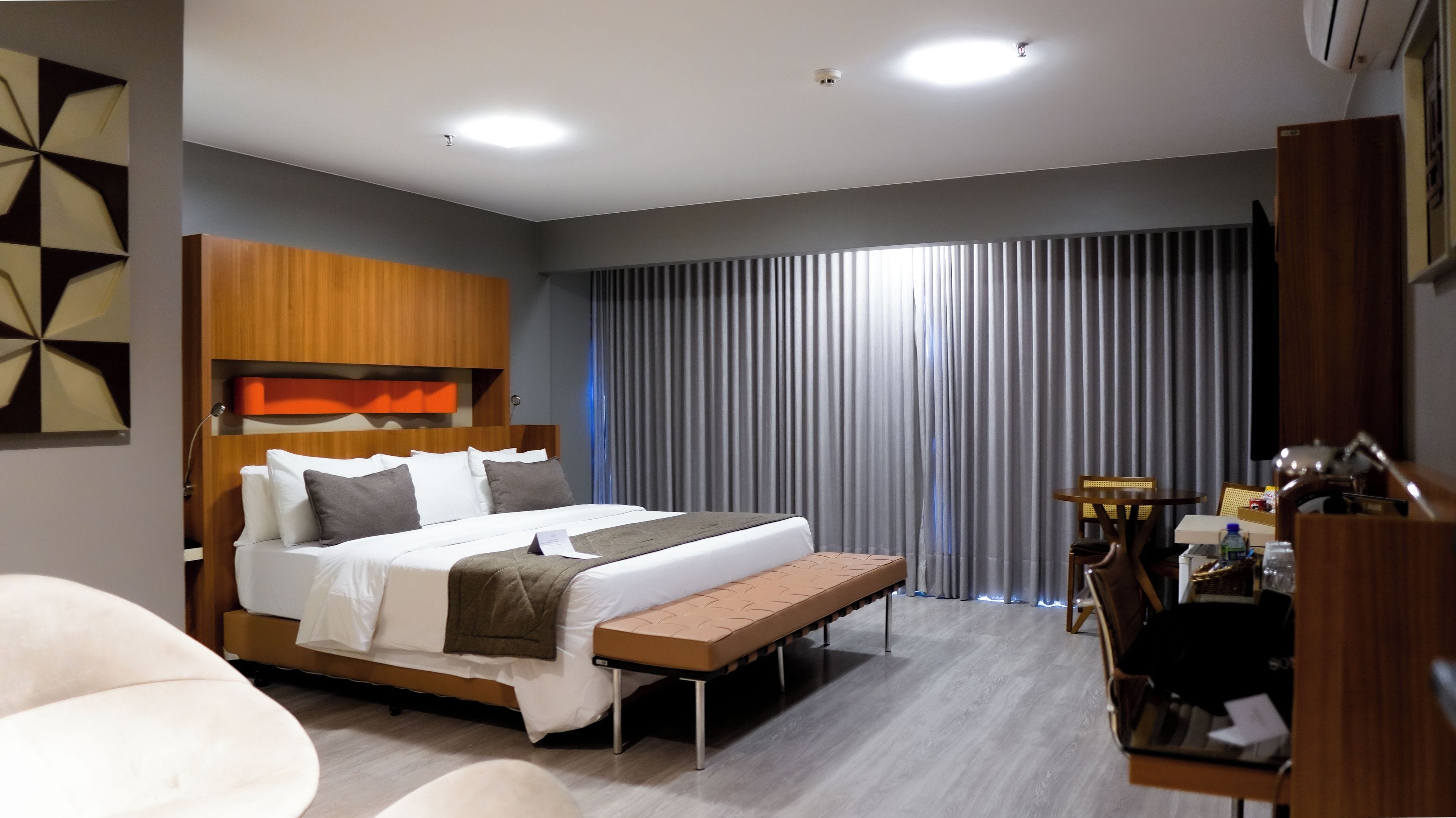 Quarto de hotel moderno com uma cama grande, uma escrivaninha e um banco.