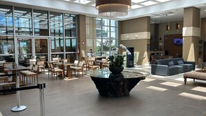 Un hall d’entrée spacieux, doté d’une table en verre au centre, entourée de sièges, de grandes fenêtres et d’un espace d’accueil.