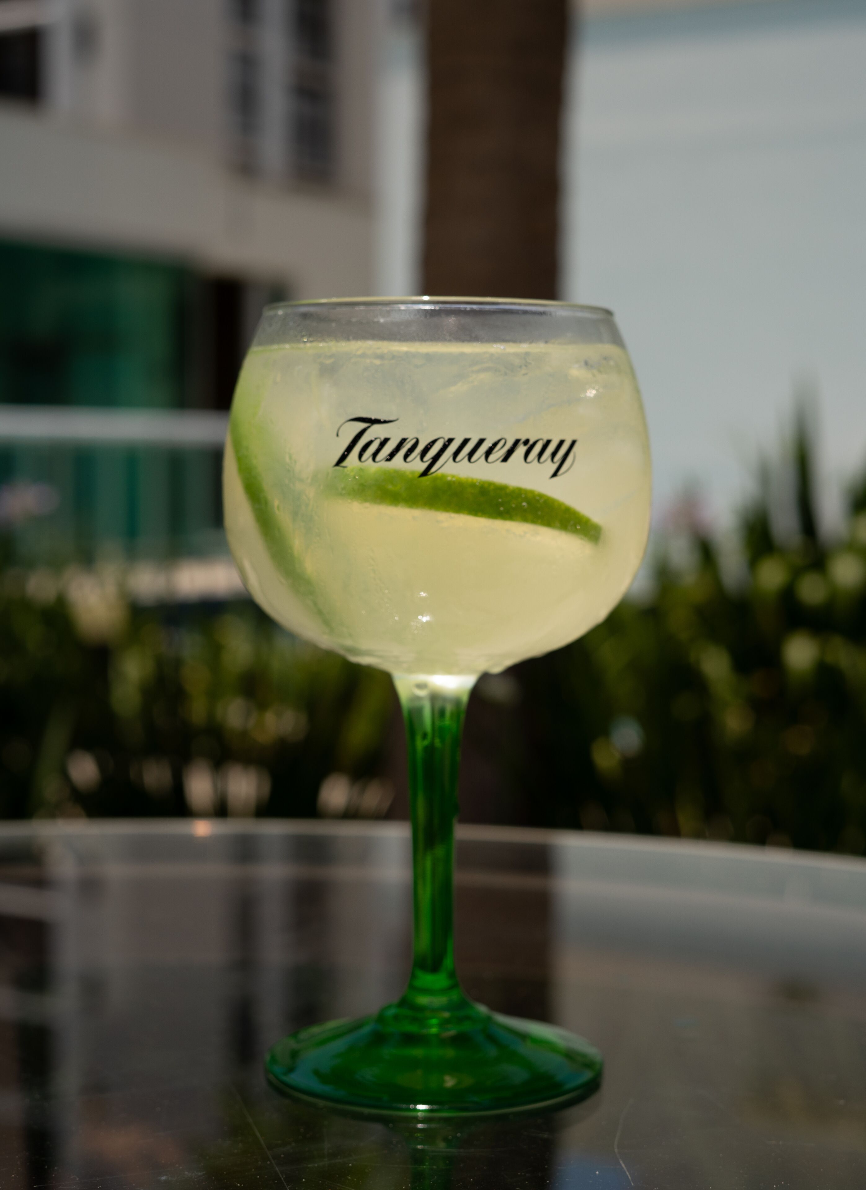 A cocktail glass labeled "Tangueray" with a lime wedge on a reflective surface.