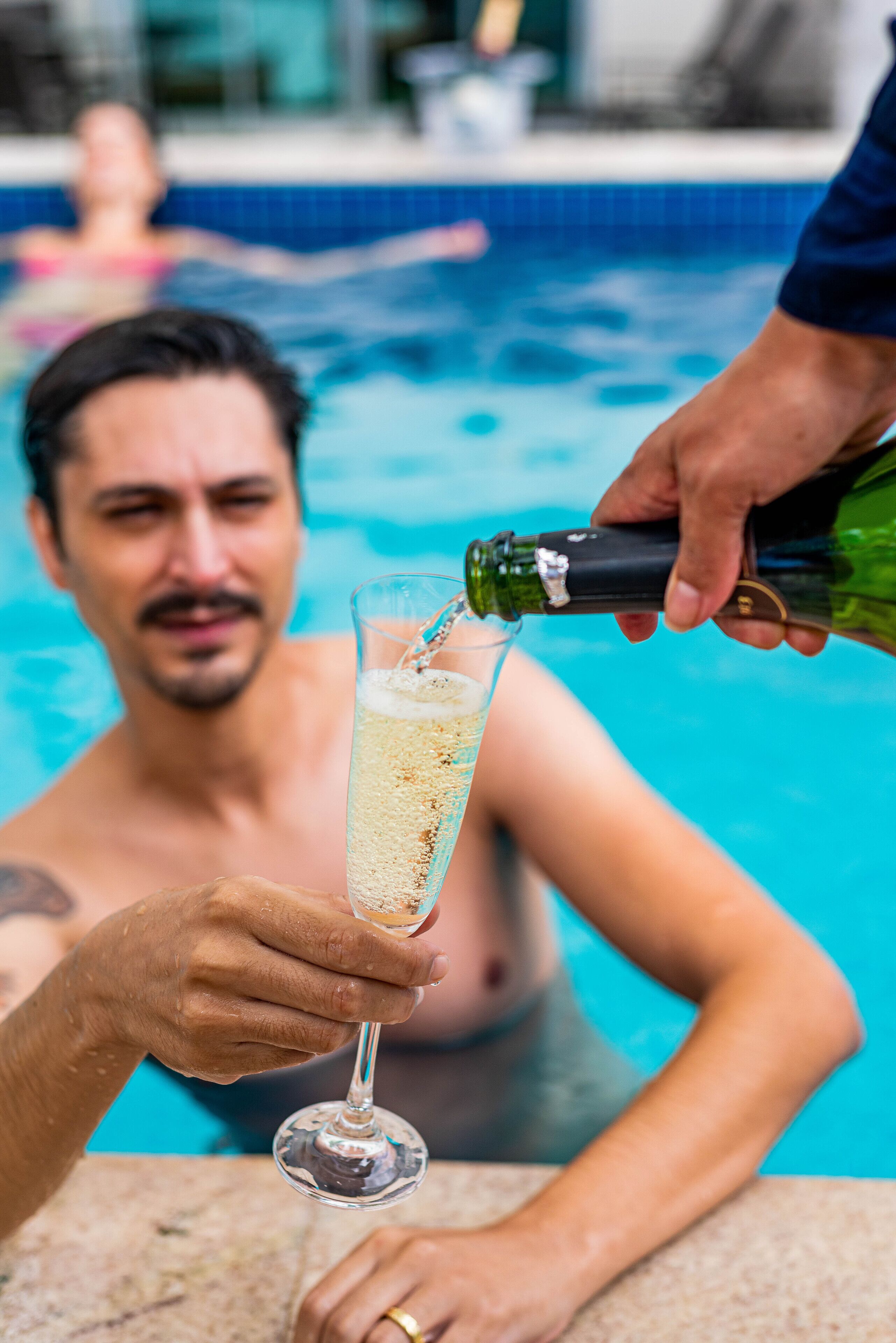 Una persona sirve champán en una copa que sostiene otra persona en una piscina.