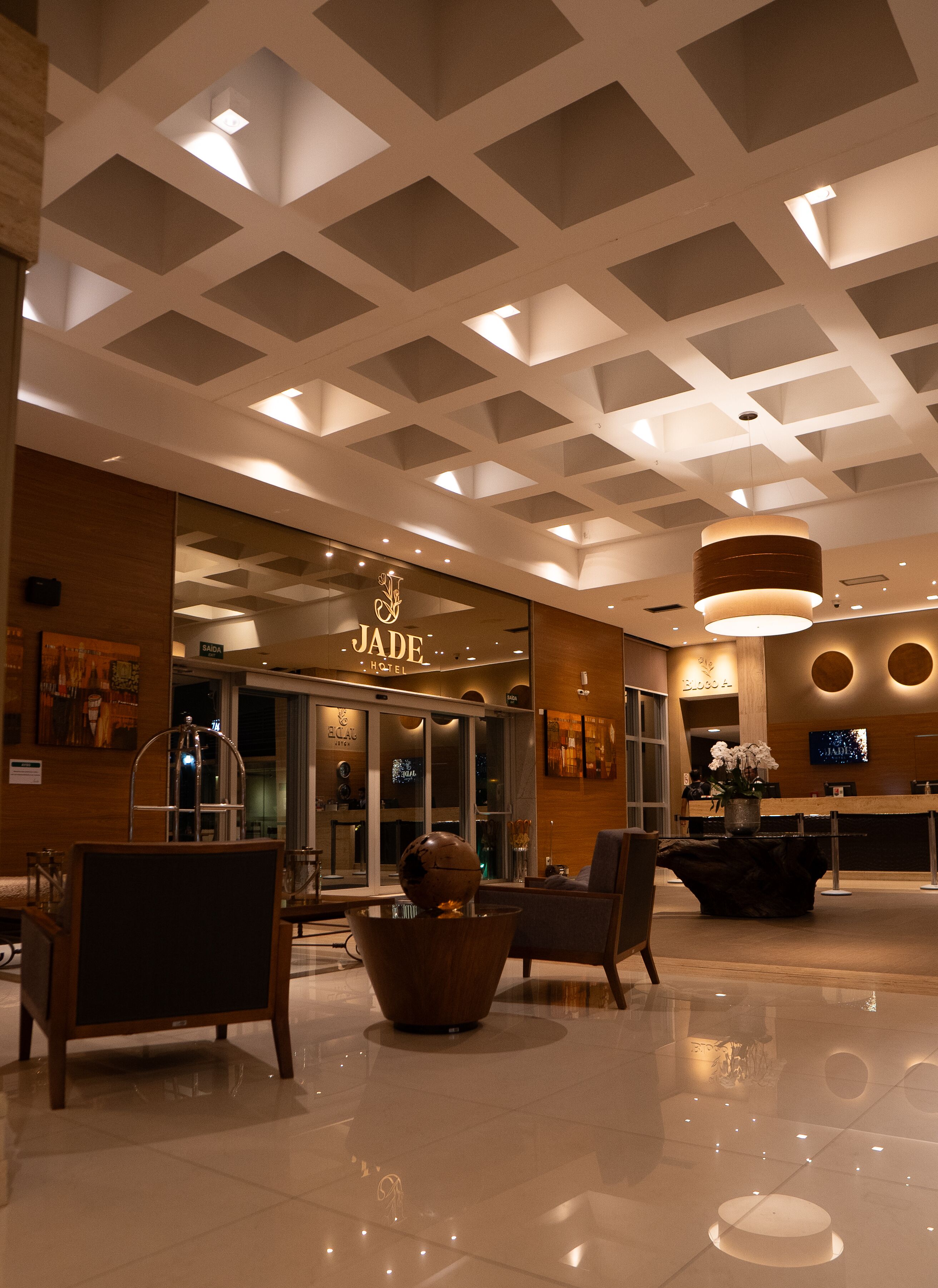 A hotel lobby with a modern ceiling design, a reception desk, and seating area.