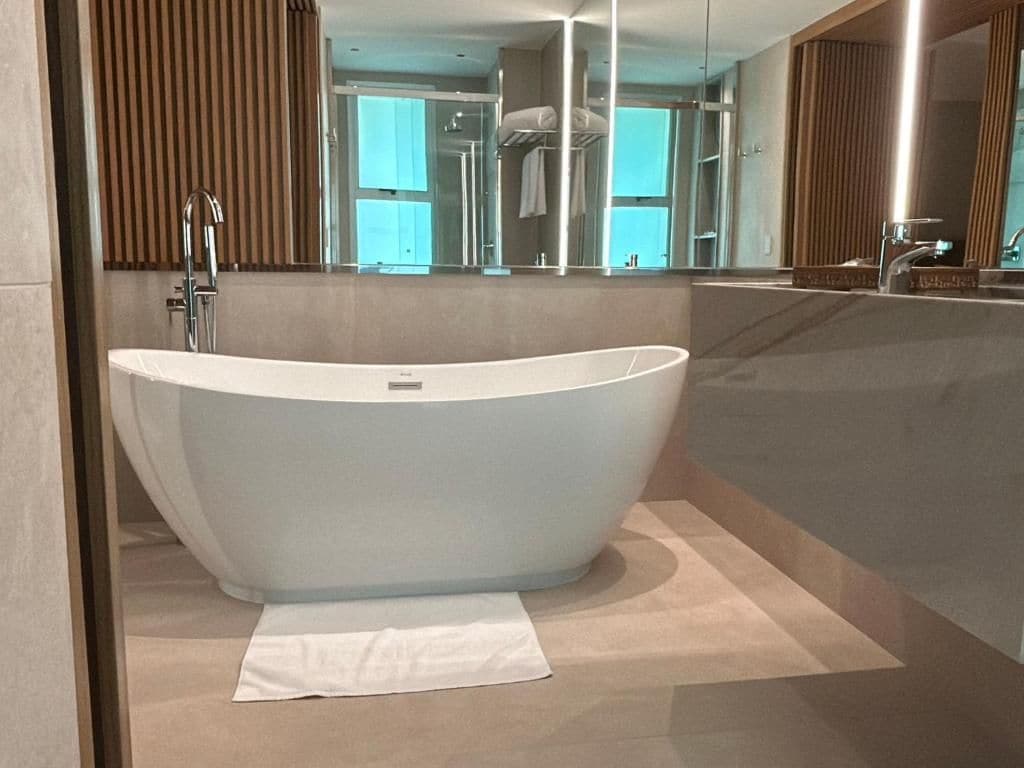 Een moderne badkamer met een vrijstaand bad, een grote spiegel en een handdoek op de vloer.