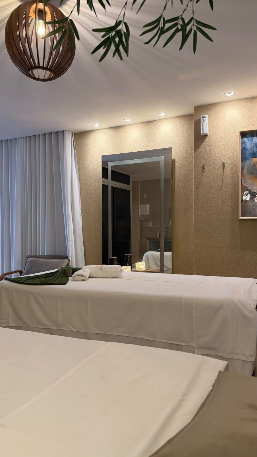 A hotel room with a bed, a chair, a bedside table, a mirror, and a hanging light fixture.