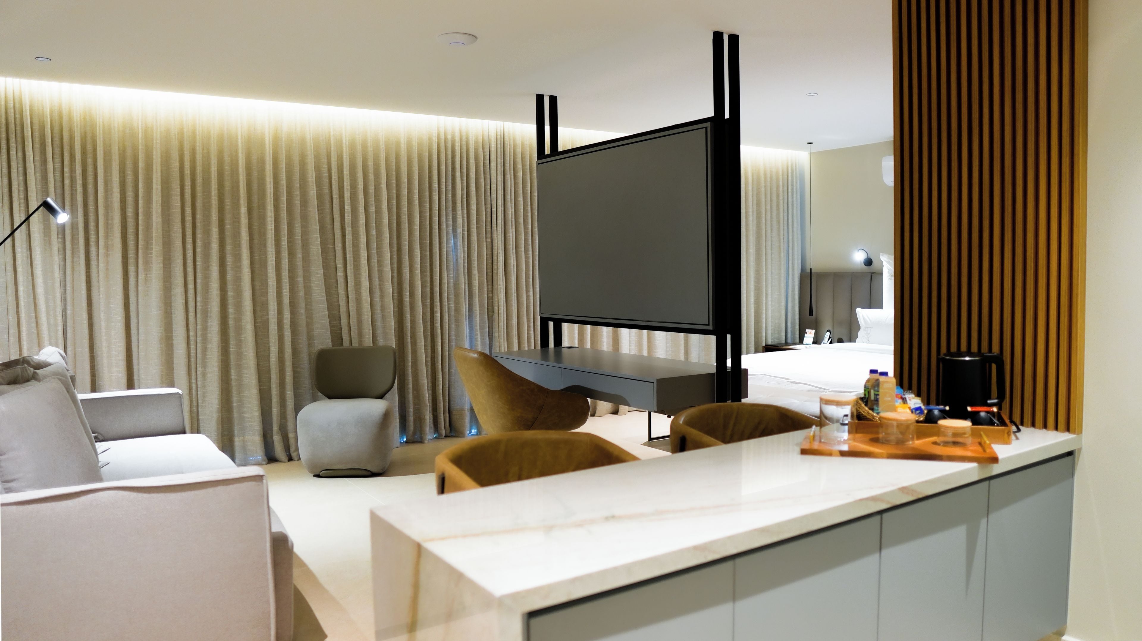 Una habitación de hotel moderna con televisión de pantalla plana, un escritorio con silla, una cama y un minibar.