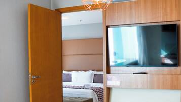 Una habitación de hotel moderna con una mesa de comedor de madera, una cama con cabecero, un televisor montado en la pared y aire acondicionado en el techo.