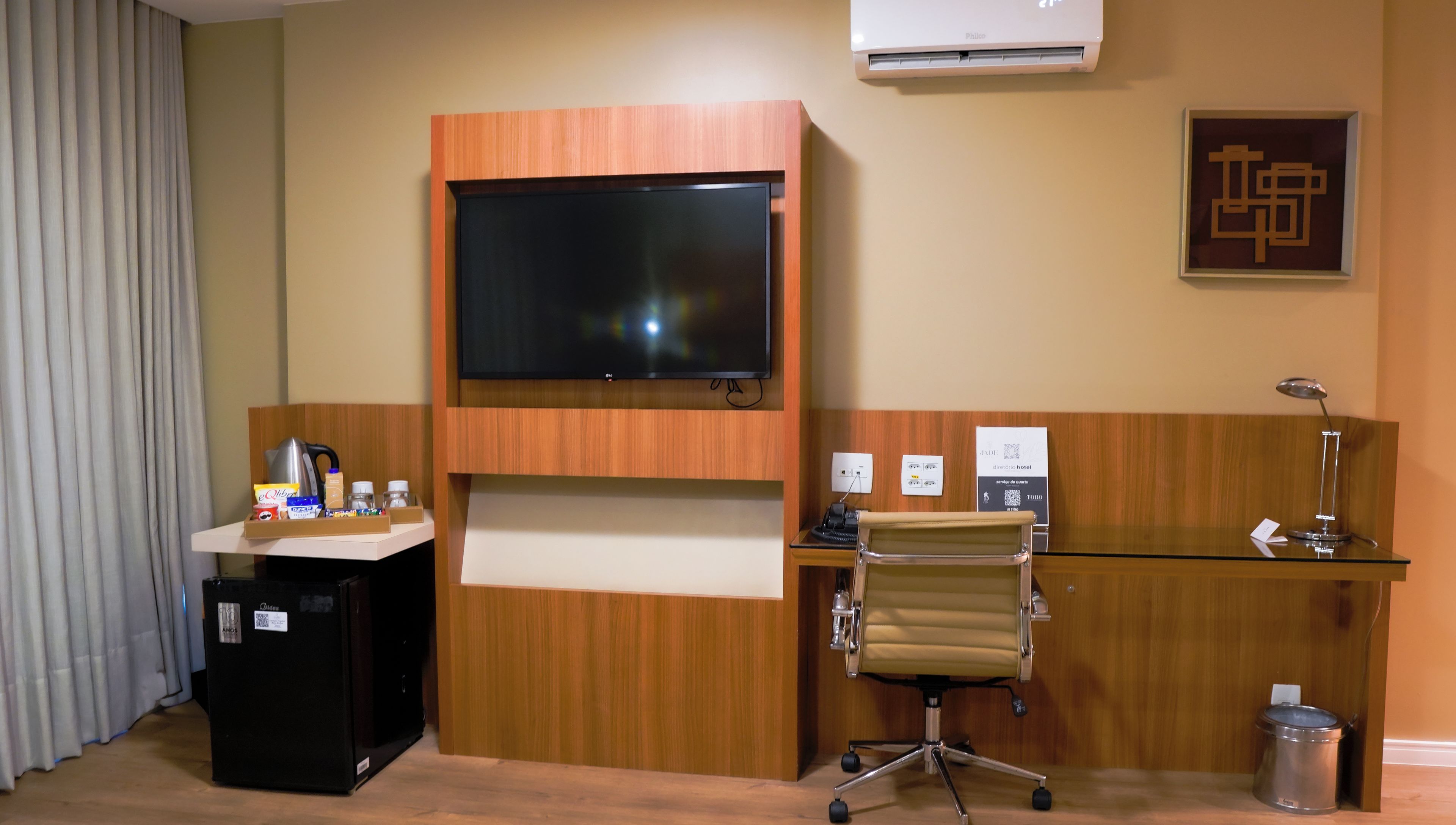 A hotel reception desk with a flat-screen TV, a telephone, a desk lamp, and a chair.