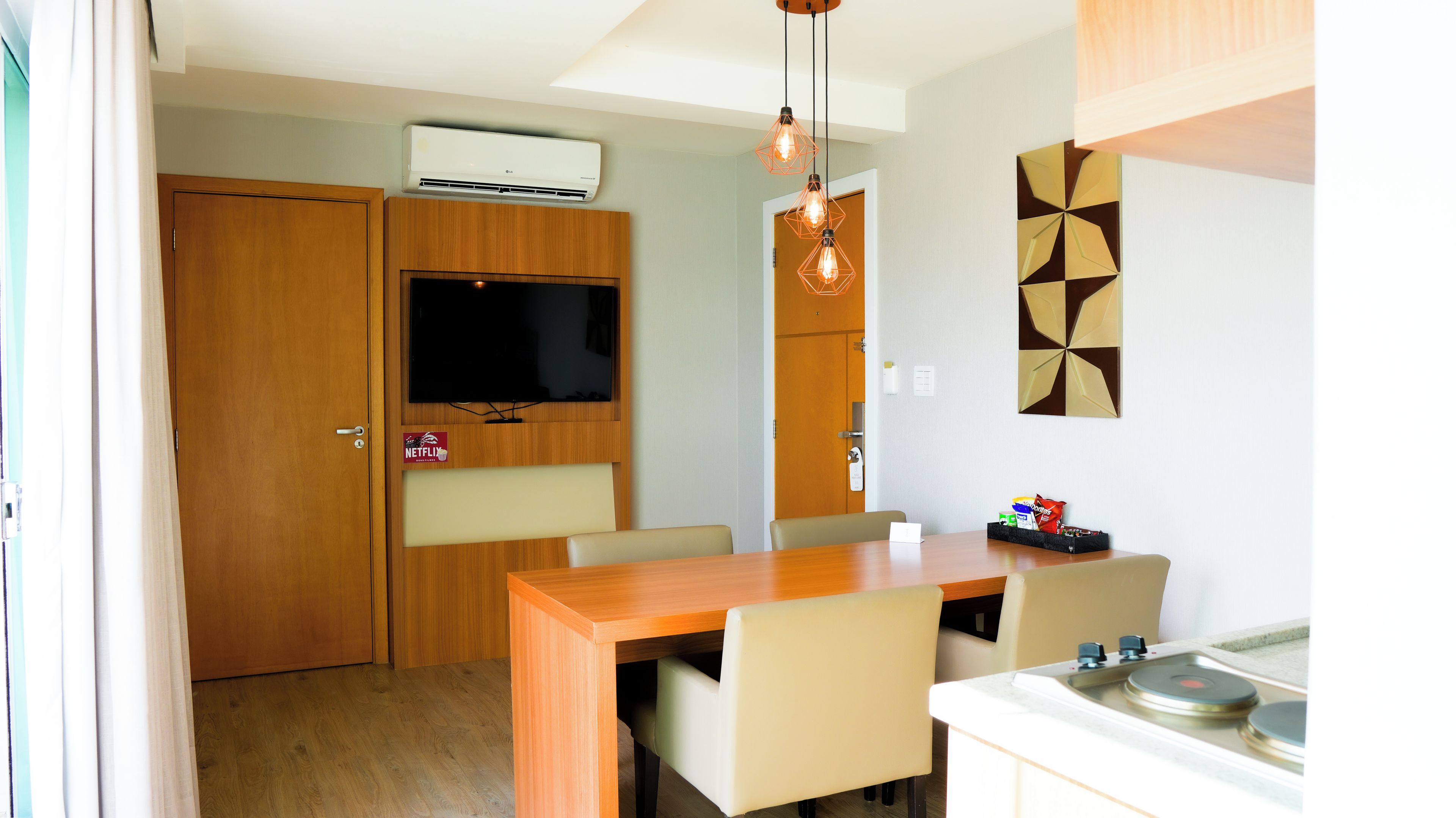 A compact kitchen with a dining area, a built-in TV, and a wall-mounted air conditioner.