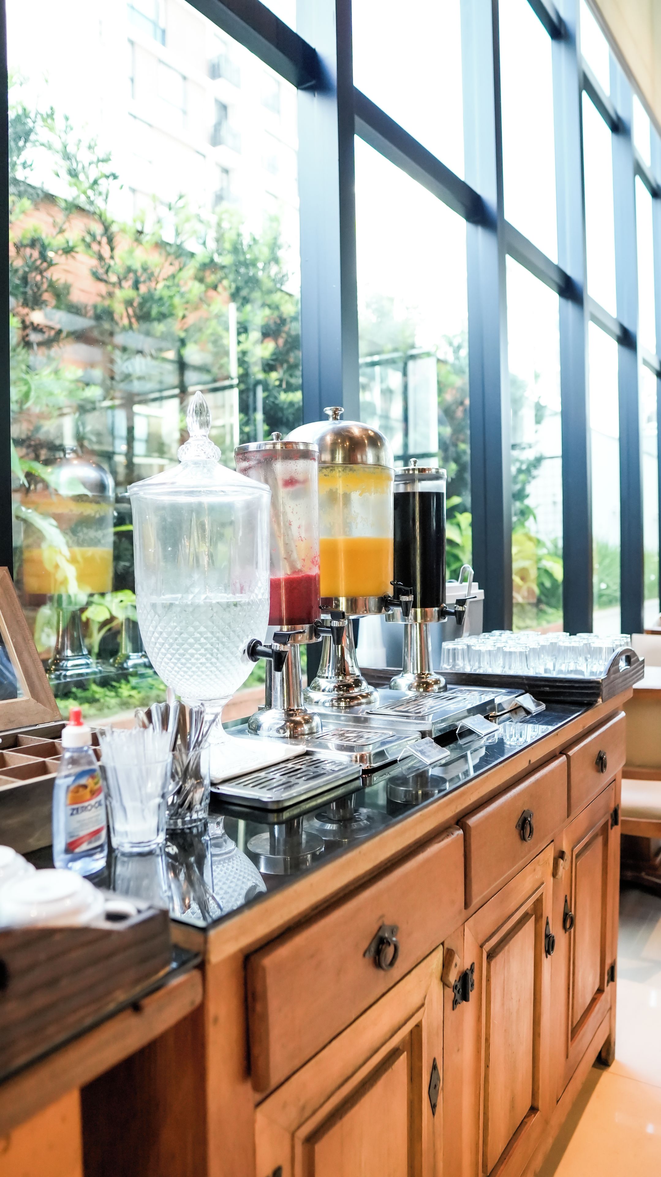 A bar area with a beverage dispenser, glasses, and a bottle of hand sanitizer.
