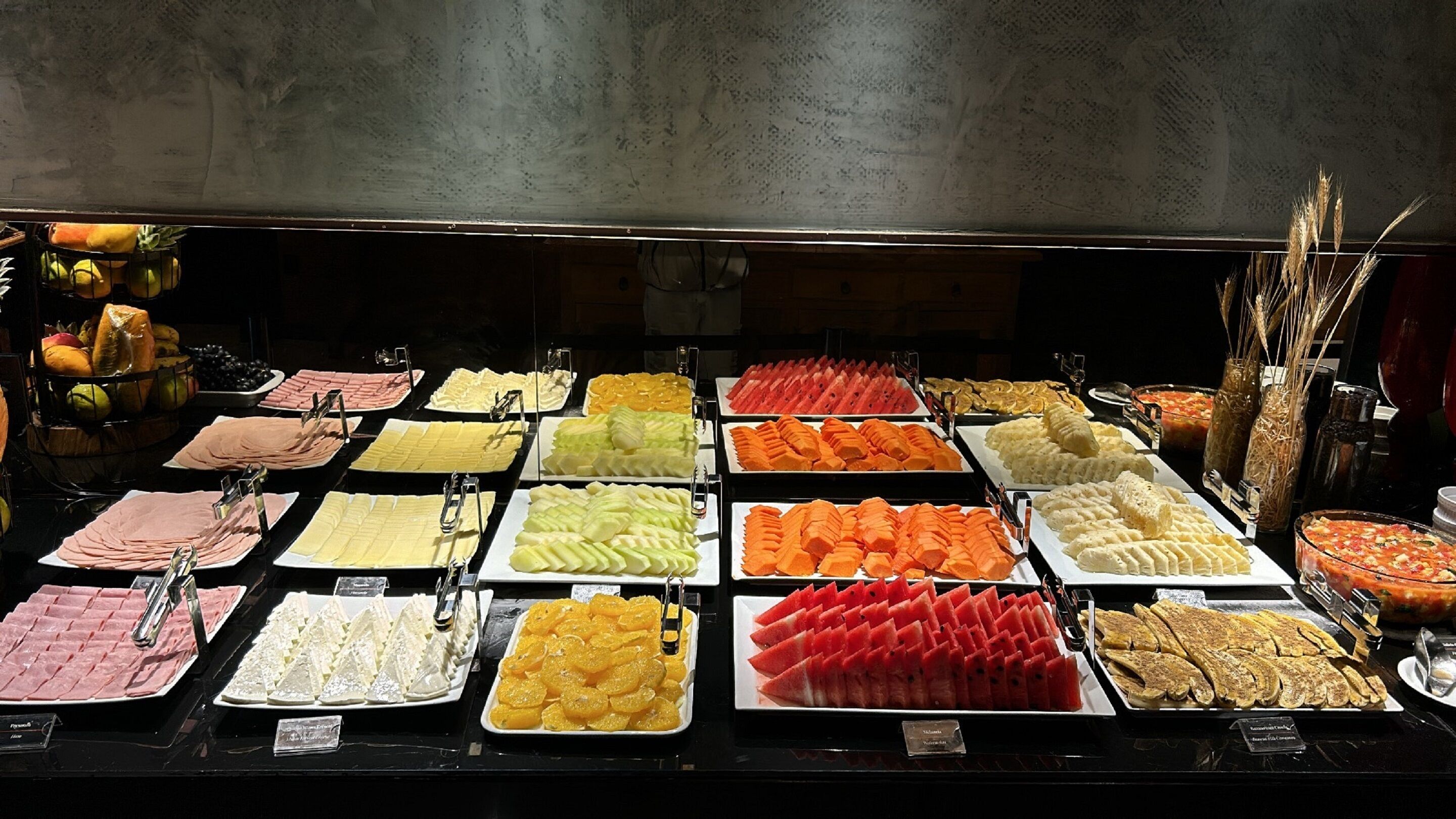 Un bufé con diversos alimentos, entre ellos frutas, quesos y embutidos.