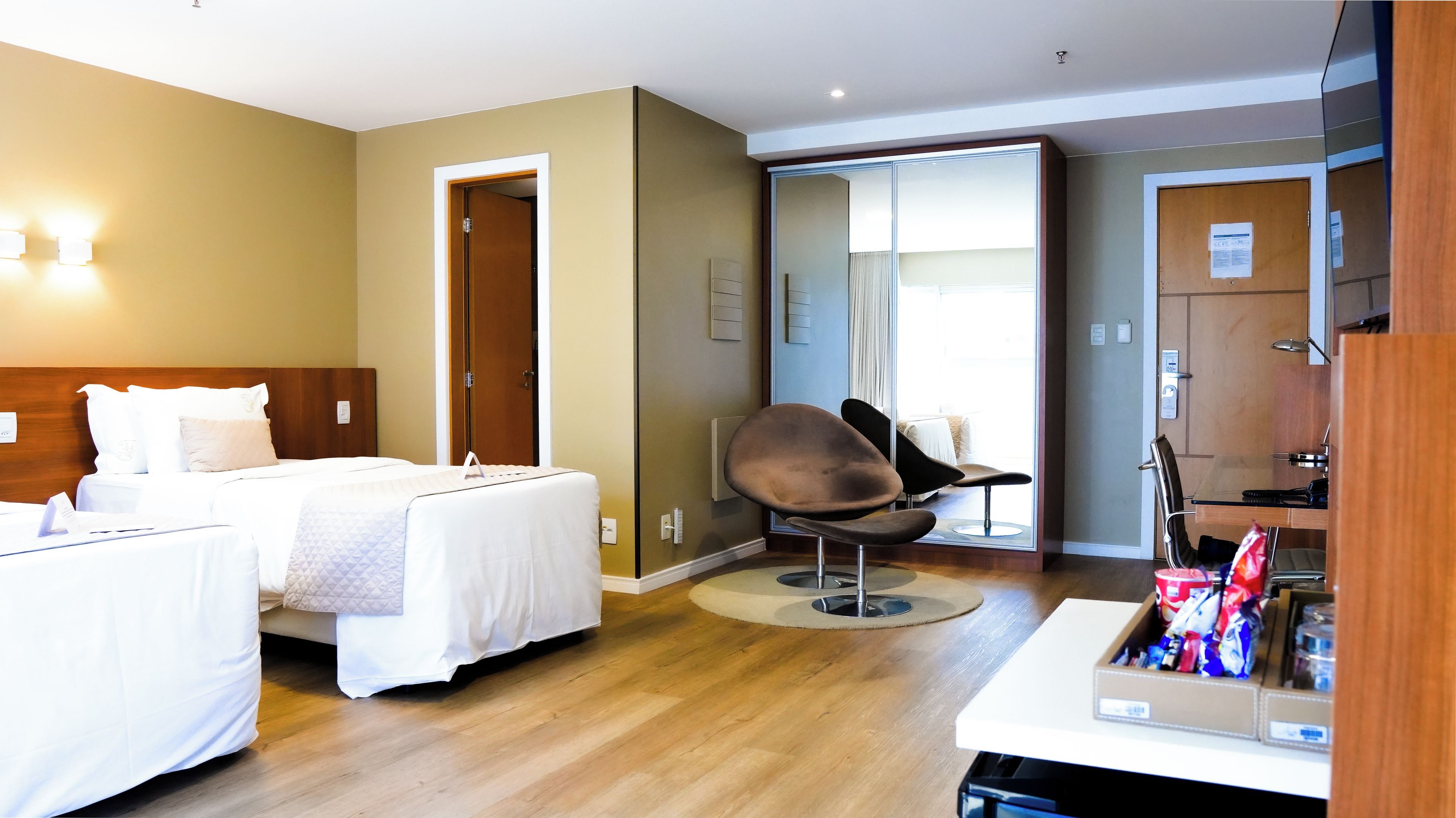 Habitación de hotel con dos camas, una silla, un escritorio y un minibar.