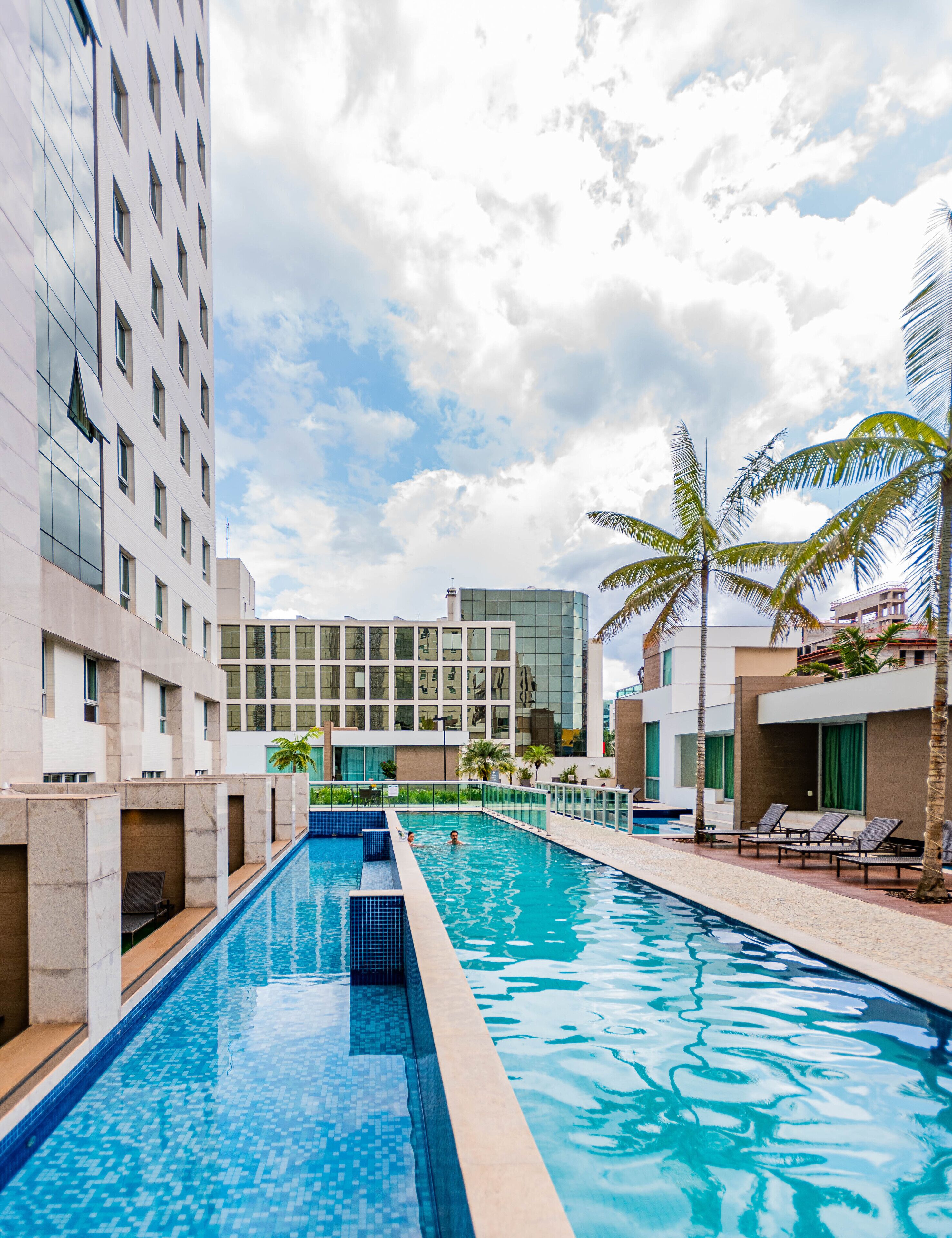 Um hotel moderno com piscina, vários andares e arquitetura que combina vidro e concreto.