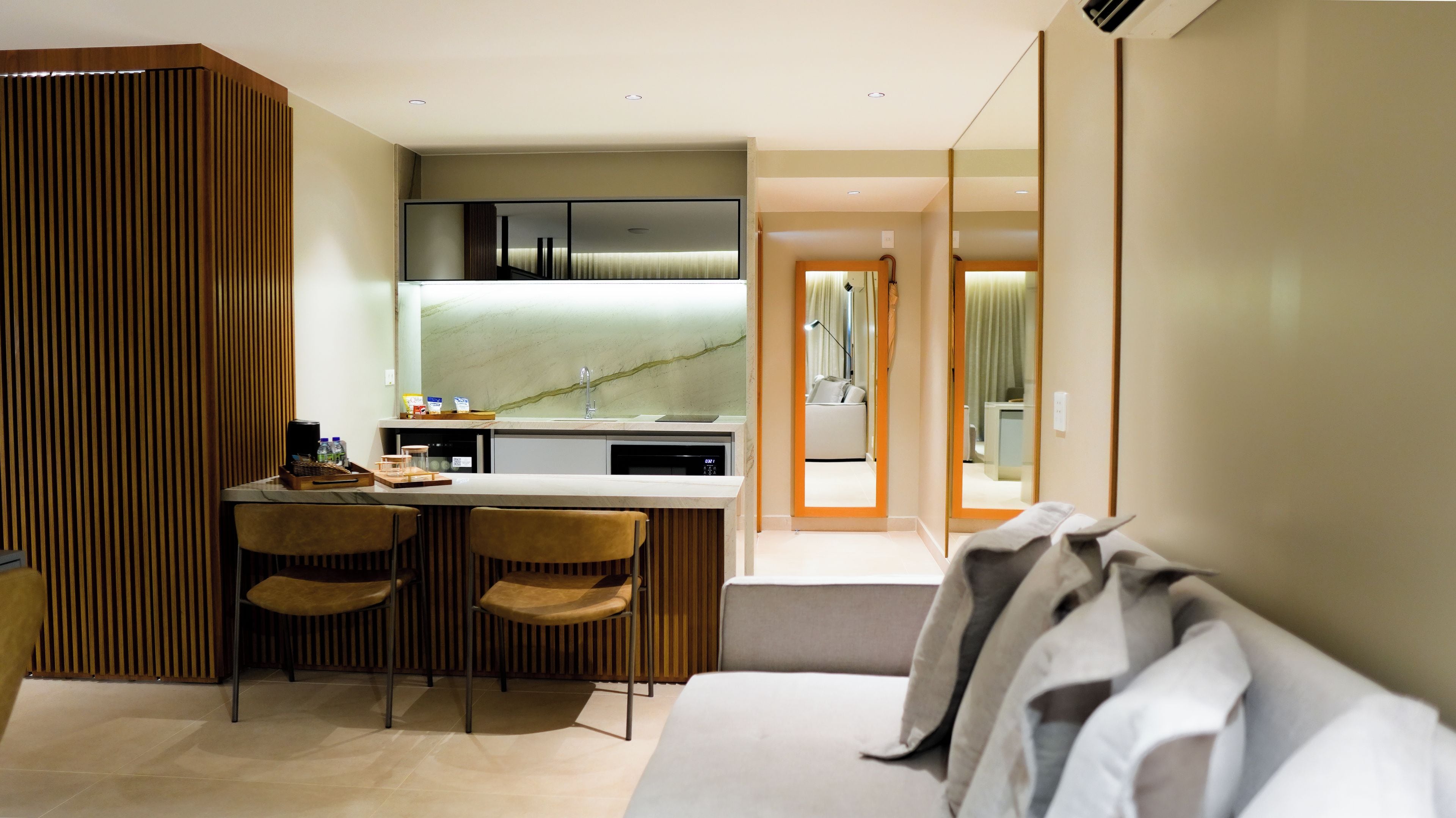 Quarto de hotel moderno com cozinha compacta, sofá e espelho.
