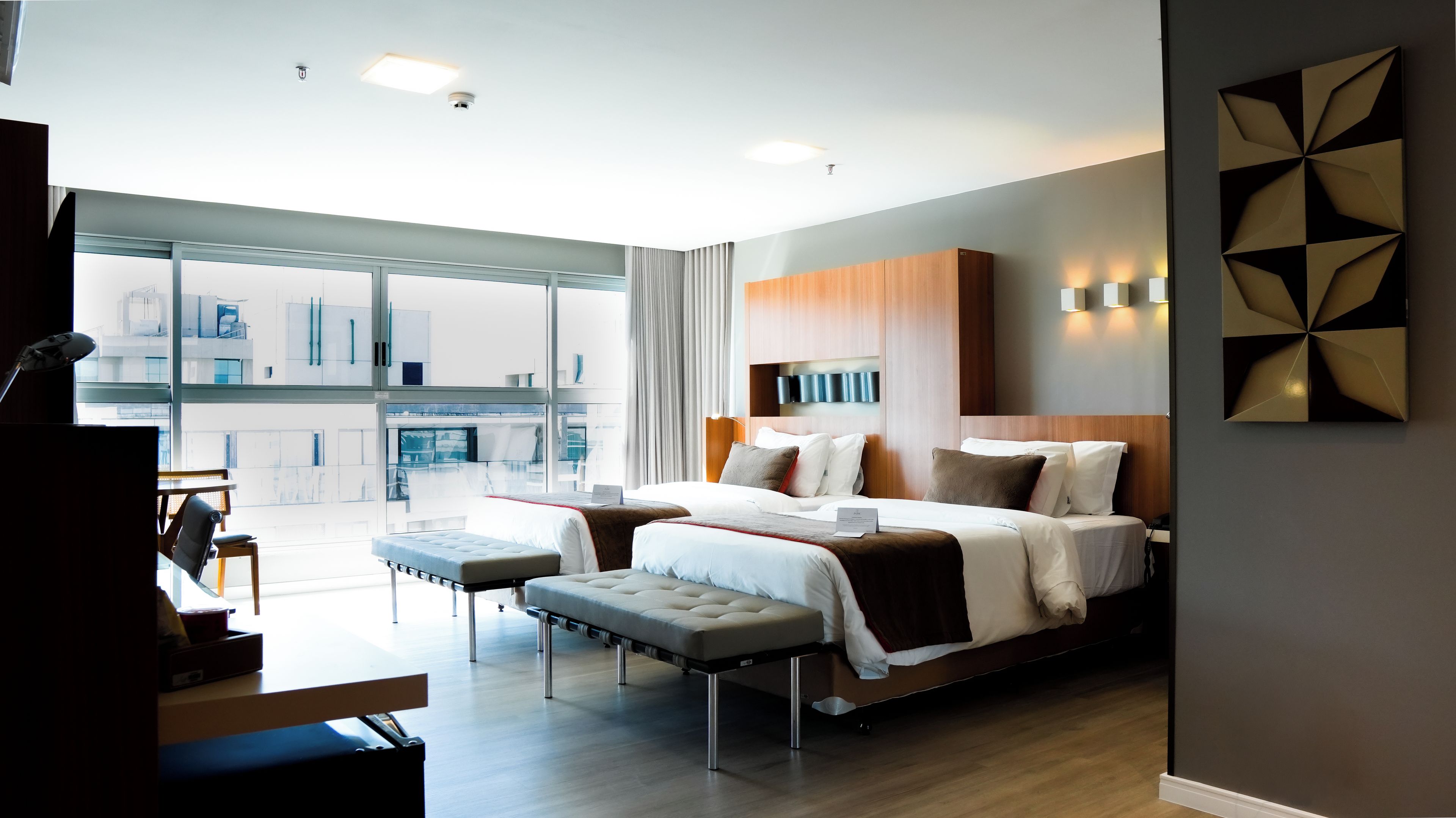 Ein modernes Hotelzimmer mit einem großen Bett, einem Schreibtisch und Blick auf die Stadt durch raumhohe Fenster.