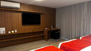 A hotel room with a wooden wall, a flat-screen TV, a small kitchenette, and two red beds.