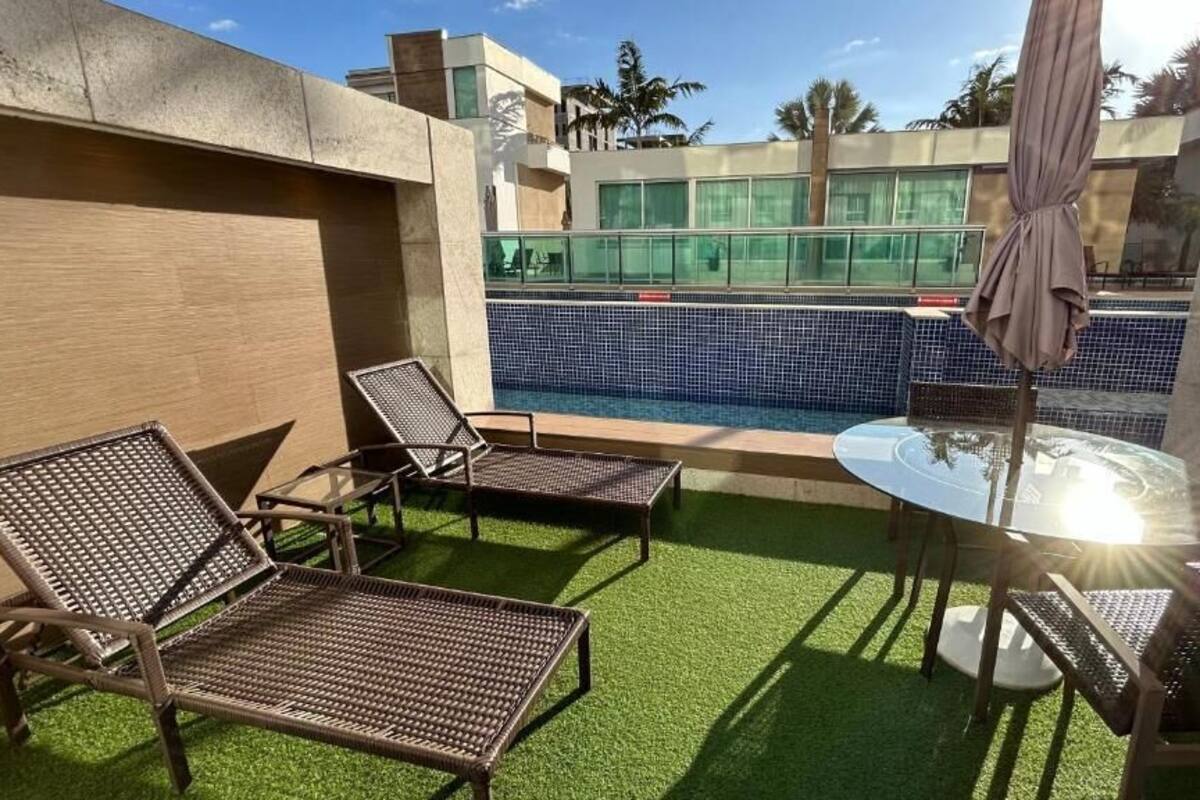 A poolside area with artificial grass, lounge chairs, and a glass table.