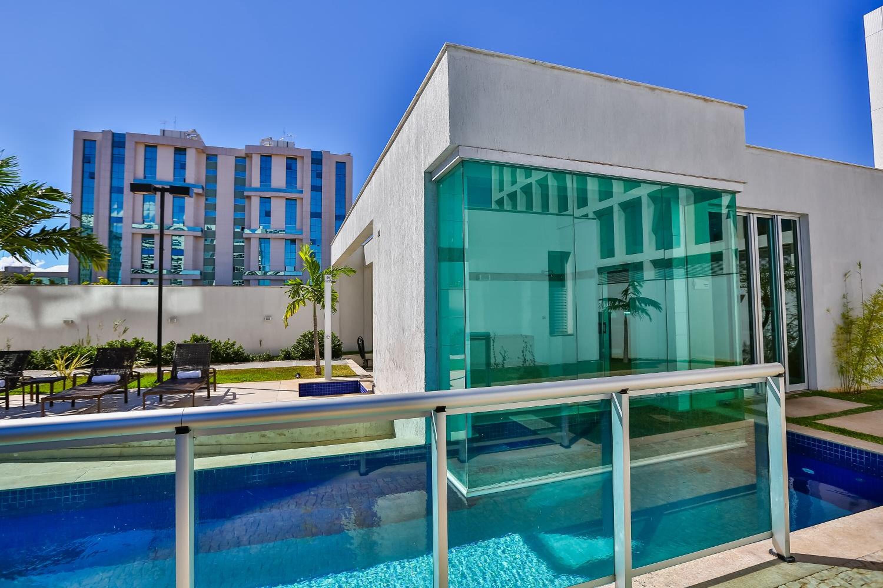 Un hôtel moderne doté d’un espace piscine entièrement vitré, de sièges en plein air et offrant une vue sur un gratte-ciel en arrière-plan.