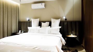 A hotel room with a large bed, a bedside table, a nightstand, an air conditioning unit, and a curtain.