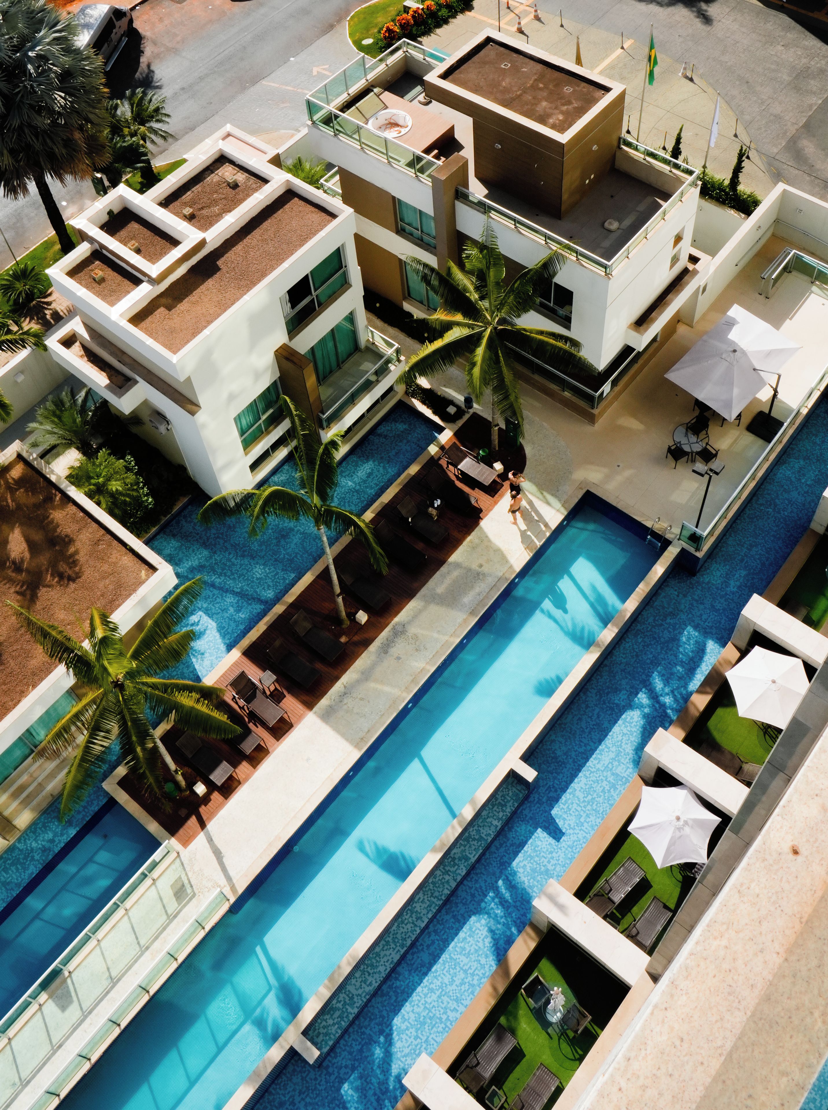 A modern hotel with a central swimming pool, outdoor seating, and palm trees.