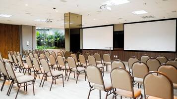 A conference room with rows of chairs, a projector screen, and a large window with a view of greenery.
